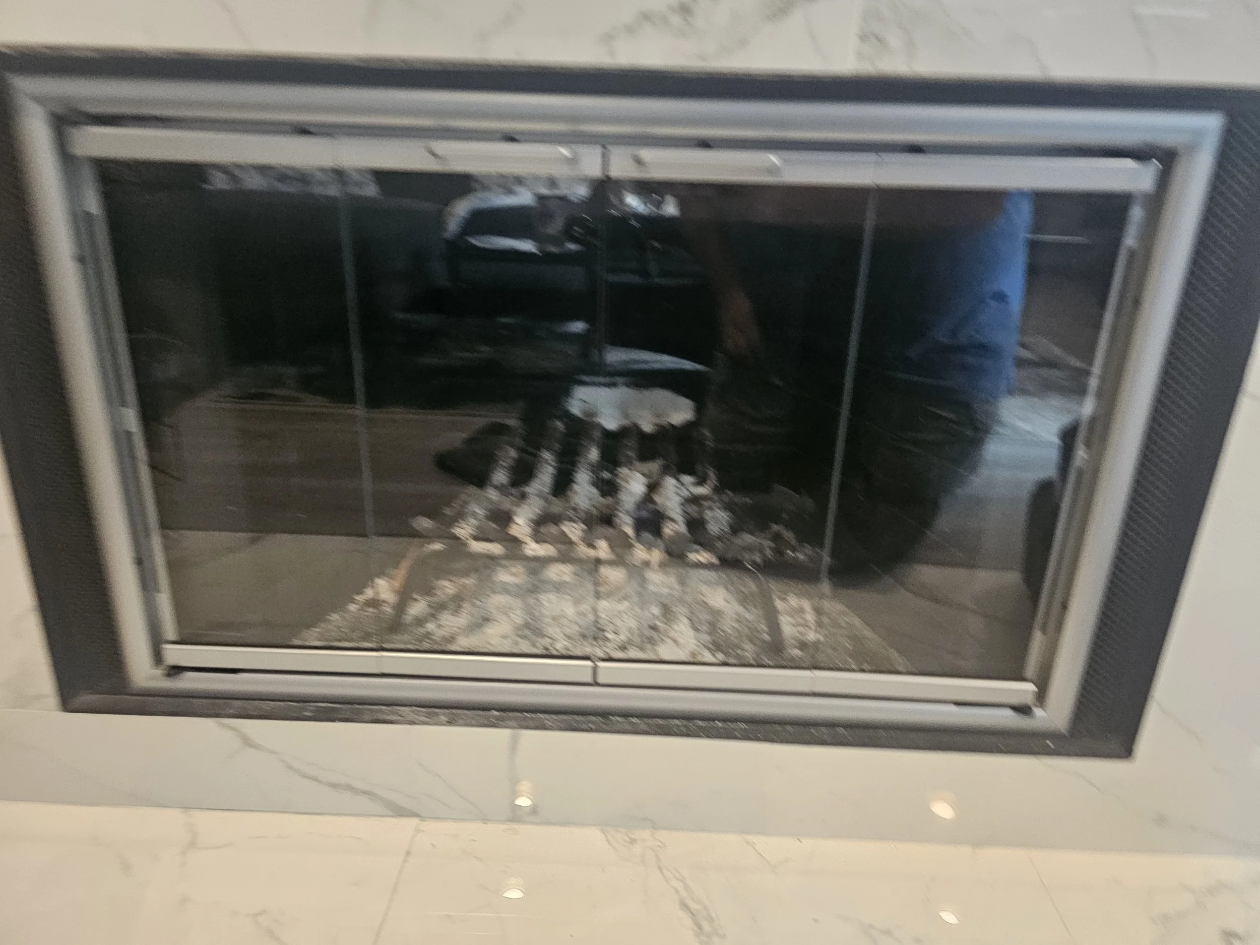 A modern glass fireplace with a black metal frame and a built-in shelf, reflecting the surroundings in the glass panes.