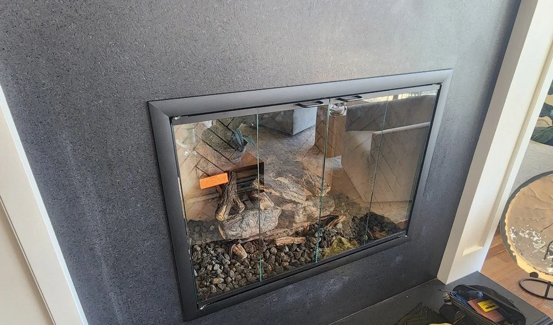 Indoor fireplace with glass doors, black frame, and stone decor inside.