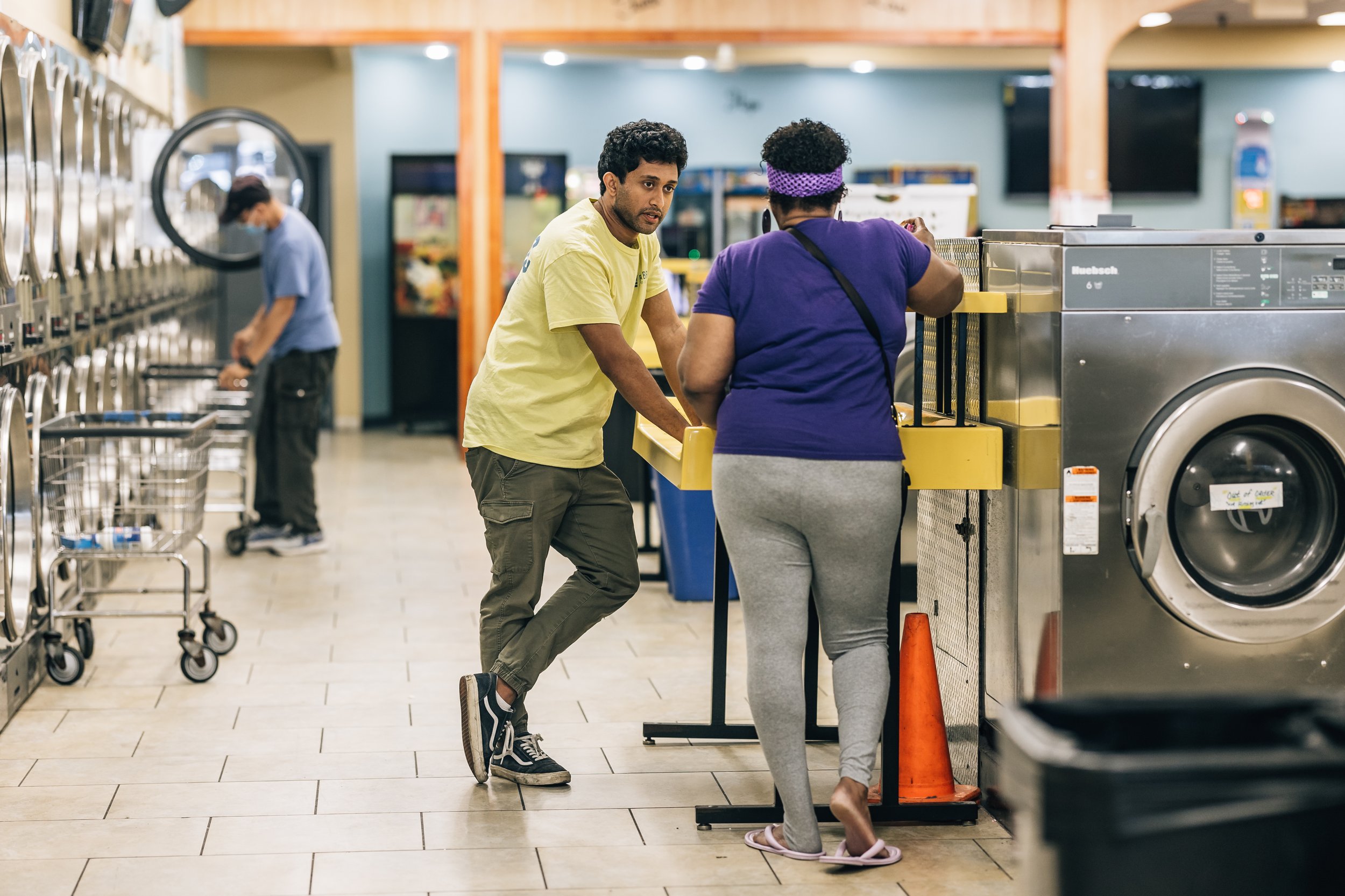 Fabric Health helping someone sign up for healthcare while doing laundry in a laundromat with washing machines and carts.