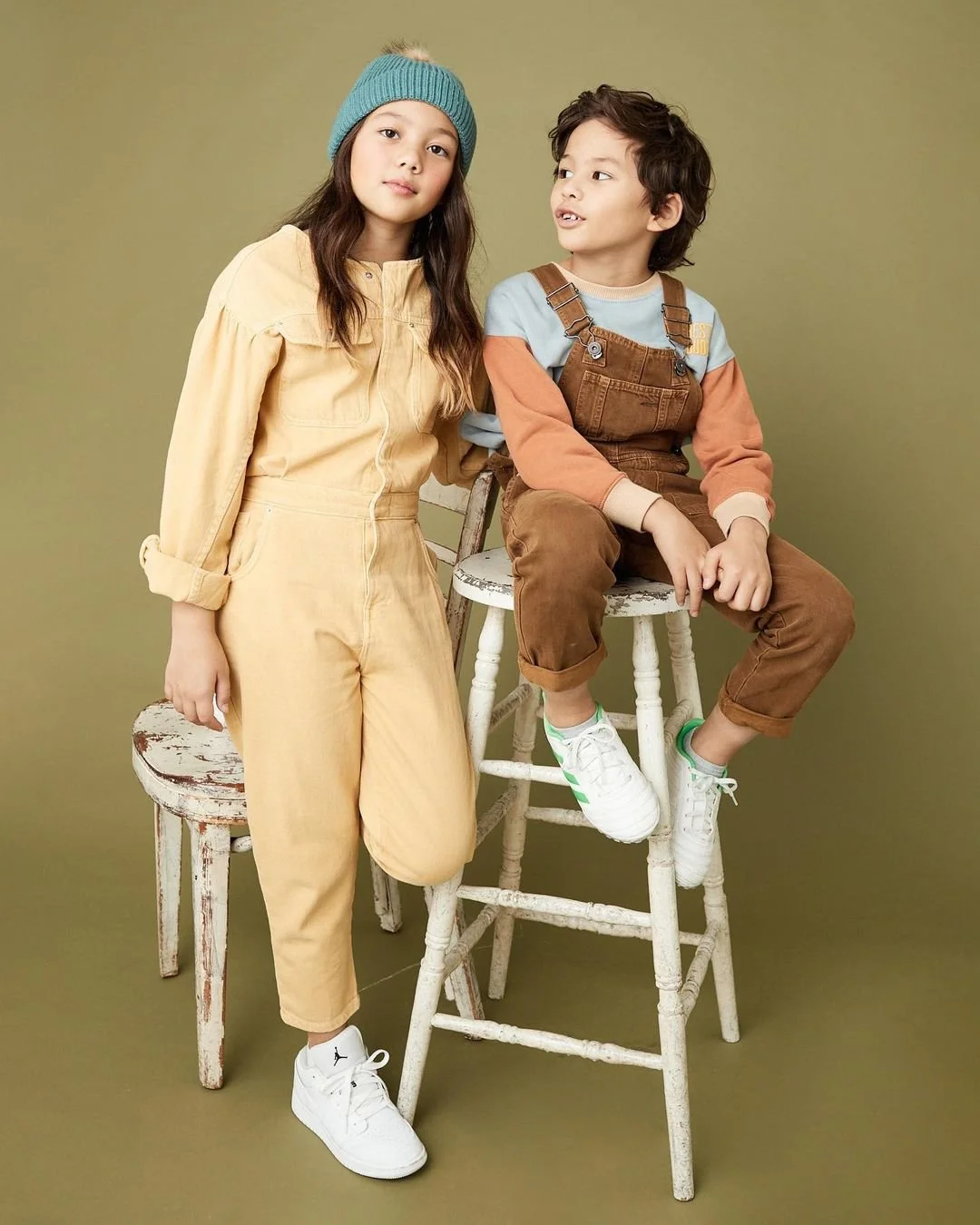 Joshua Pestka kids fashion photography — two kids in coordinating yellow and brown outfits seated on stool, olive green background