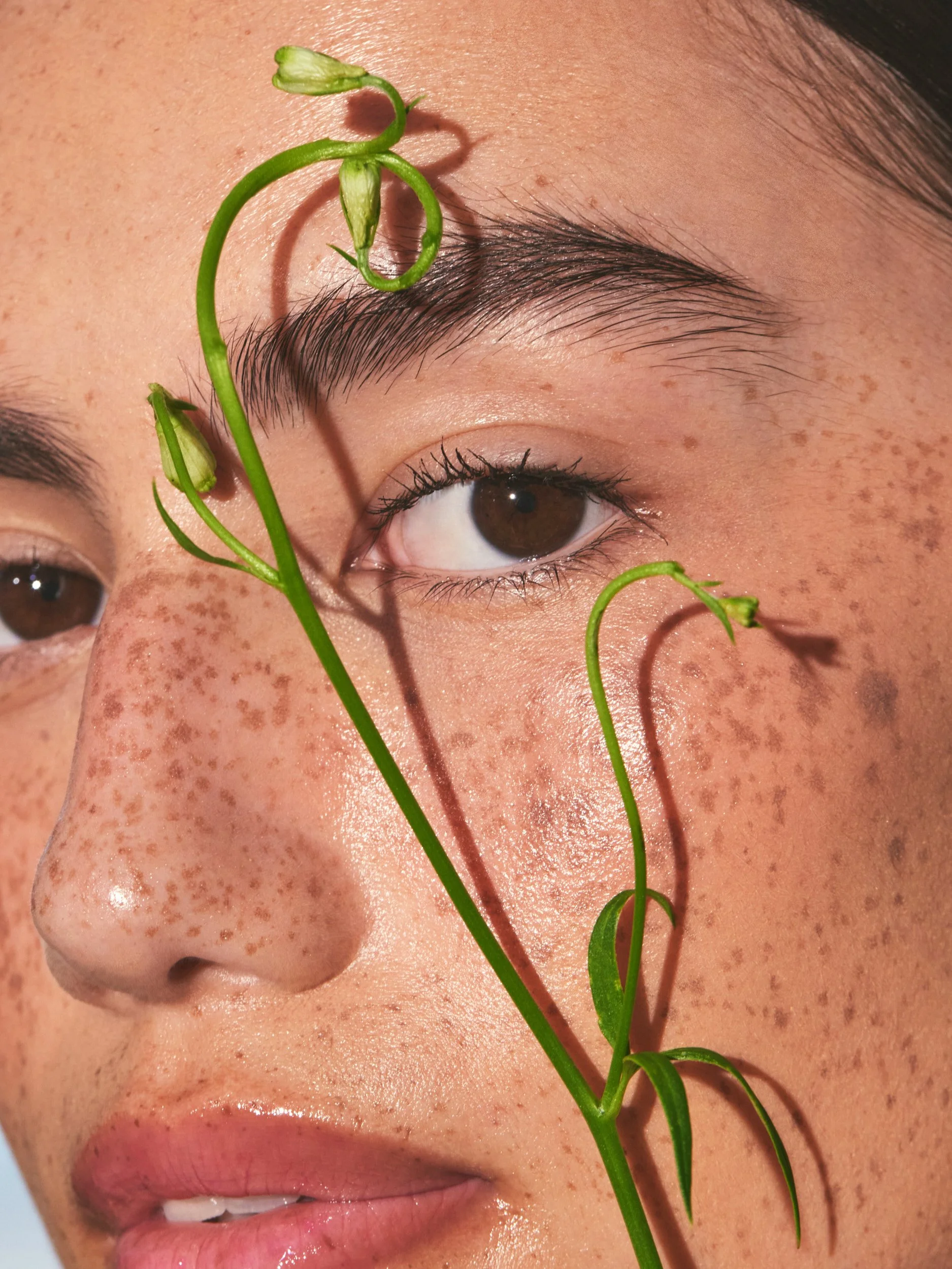 Joshua Pestka commercial beauty photography — Well People Skinphoria campaign, close-up of freckled skin with green botanical tendril, natural light