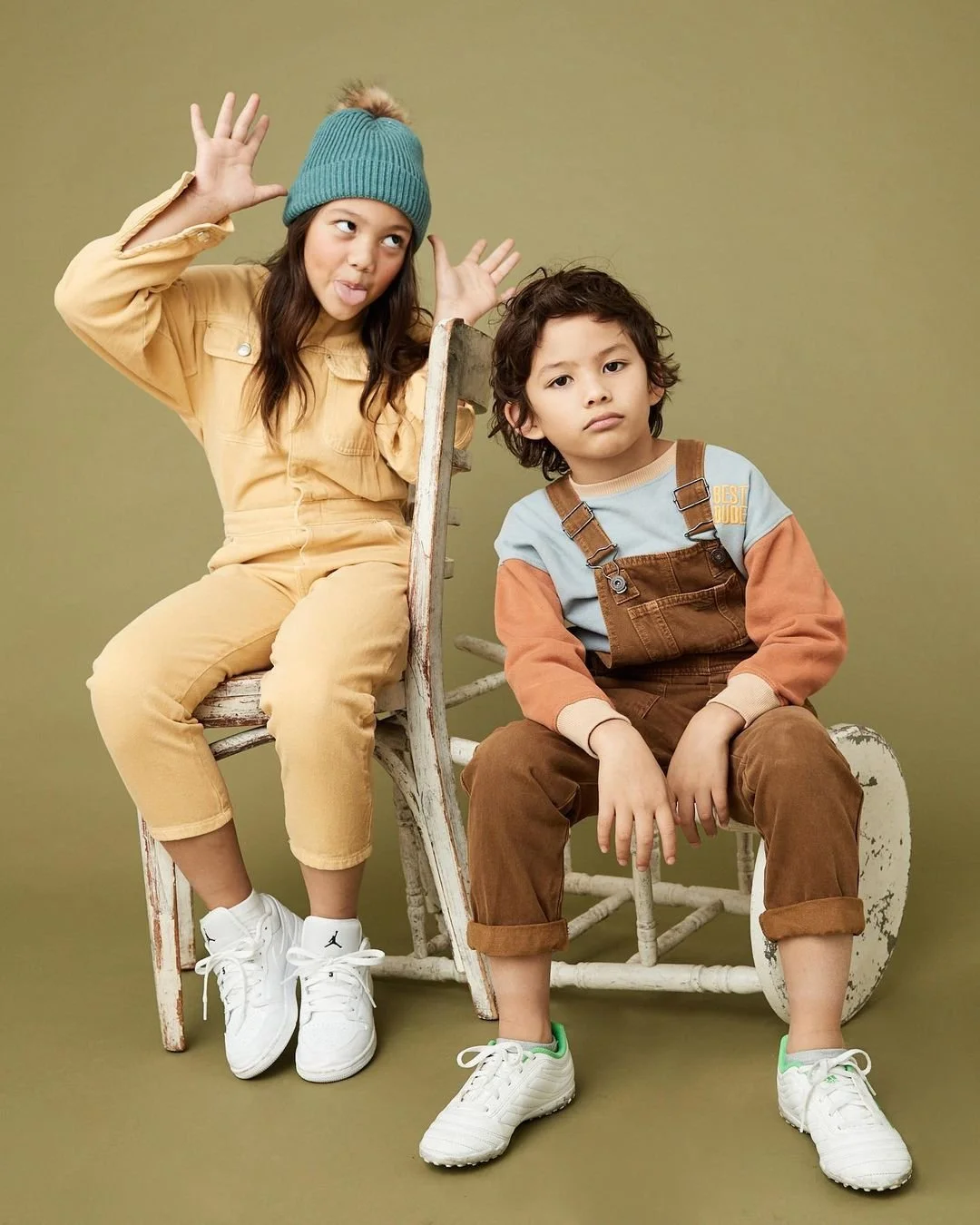 Joshua Pestka kids fashion photography — two kids in yellow and brown coordinating outfits seated on wooden stool, olive background