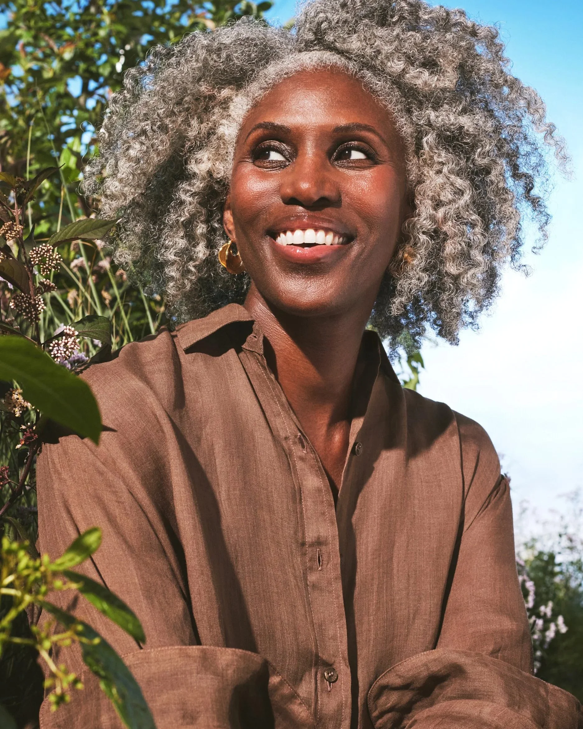 Joshua Pestka commercial beauty photography — Well People Skinphoria campaign, model with silver natural afro smiling in brown shirt, lush green background