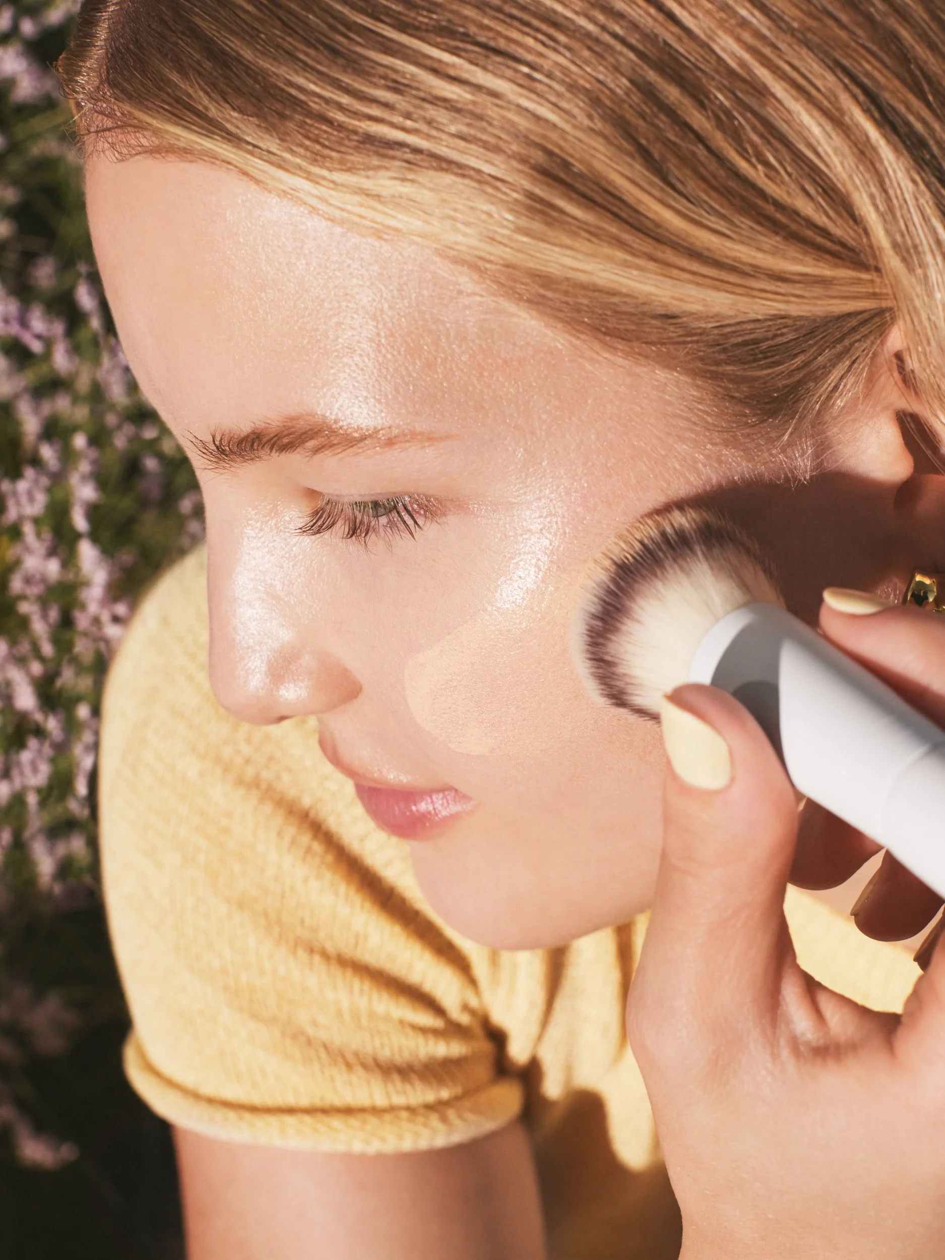 Joshua Pestka commercial beauty photography — Well People Skinphoria campaign, model applying Well People brush to cheek, close-up application shot, outdoor light