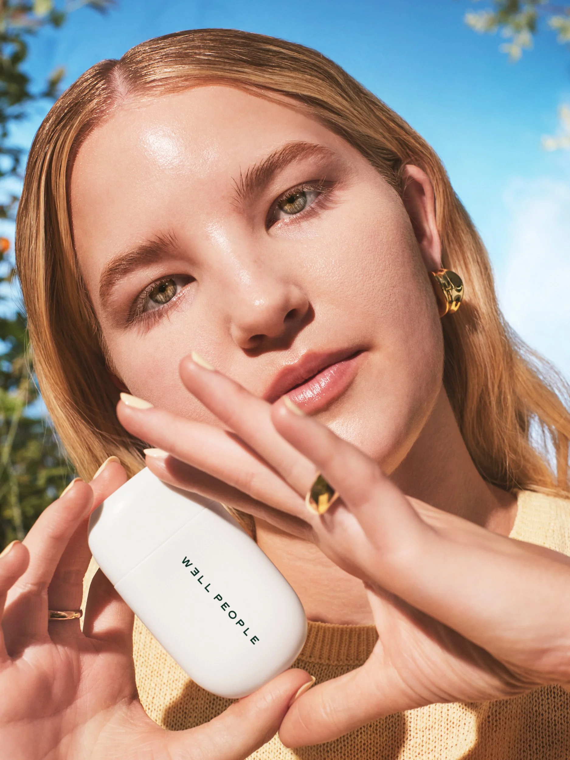 Joshua Pestka commercial beauty photography — Well People Skinphoria campaign, model holding Well People product with gold ring, luminous skin, outdoor light 