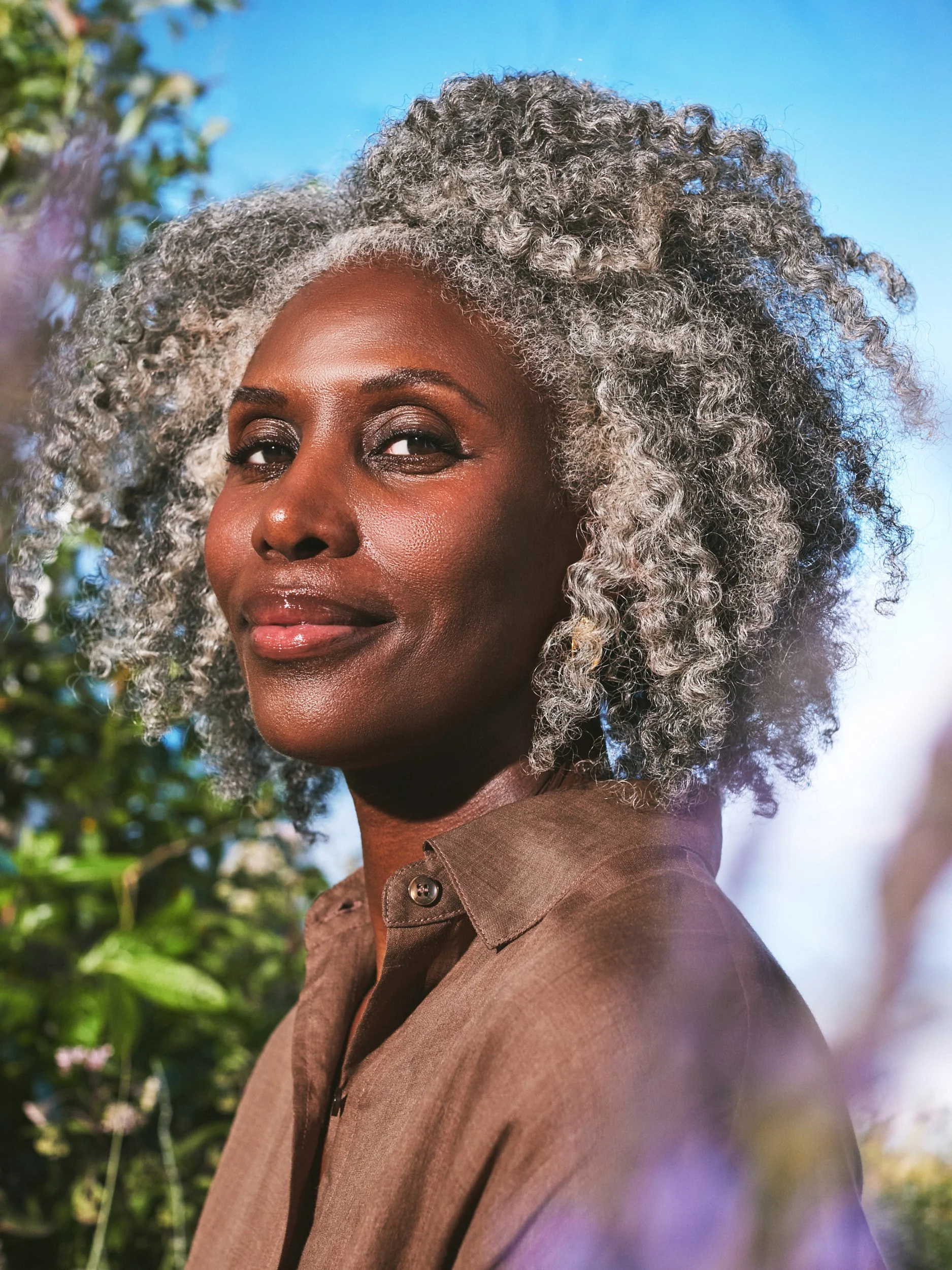 Joshua Pestka commercial beauty photography — Well People Skinphoria campaign, model with silver natural afro in brown shirt, smiling in garden setting