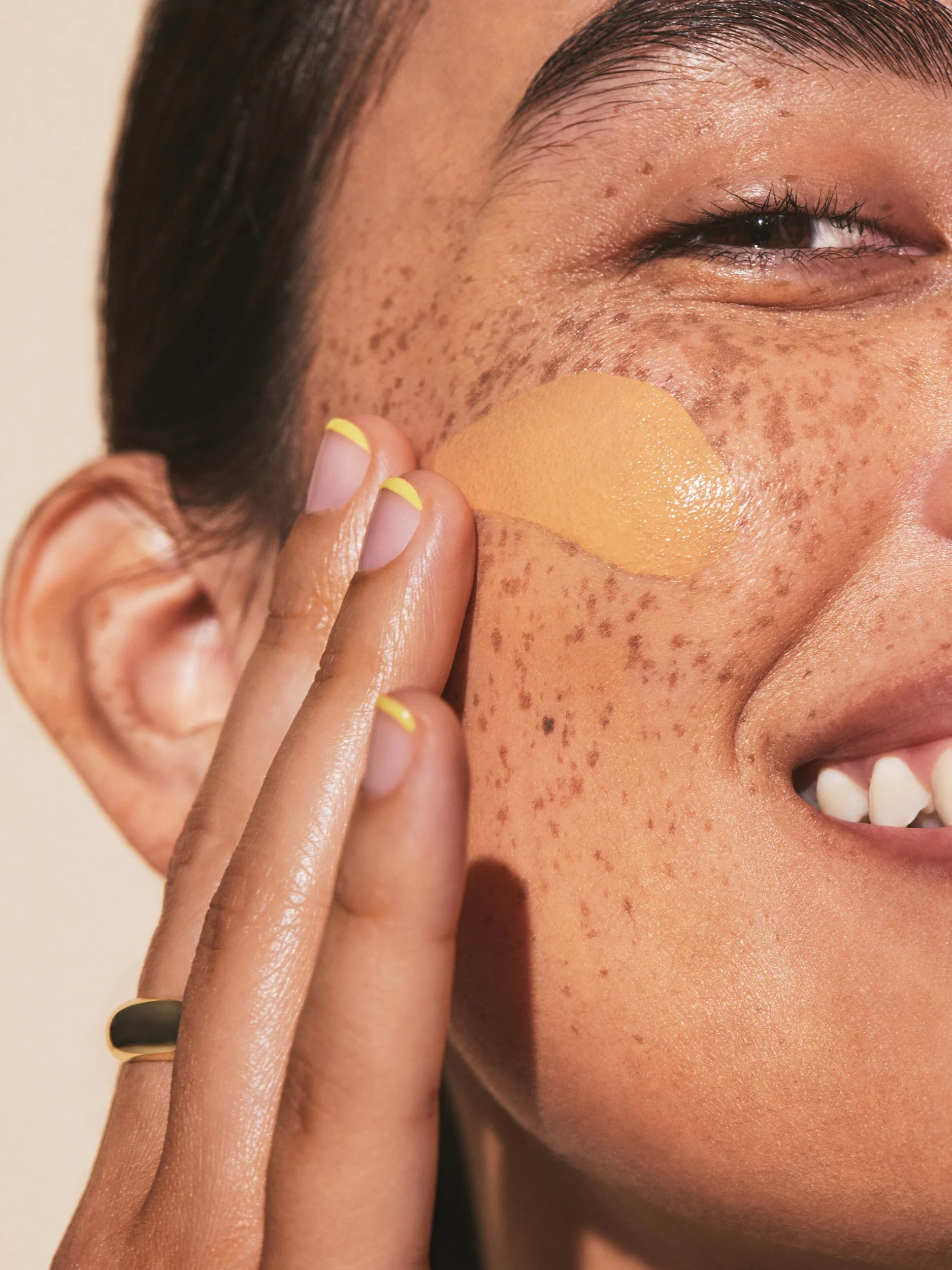 Joshua Pestka commercial beauty photography — Well People Skinphoria campaign, close-up of freckled skin with product swatch on cheek, hand detail and yellow nails