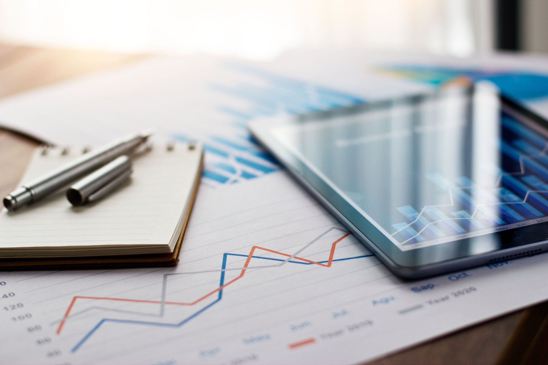 Business workspace with financial charts, a tablet, a notebook, and pens on a desk.