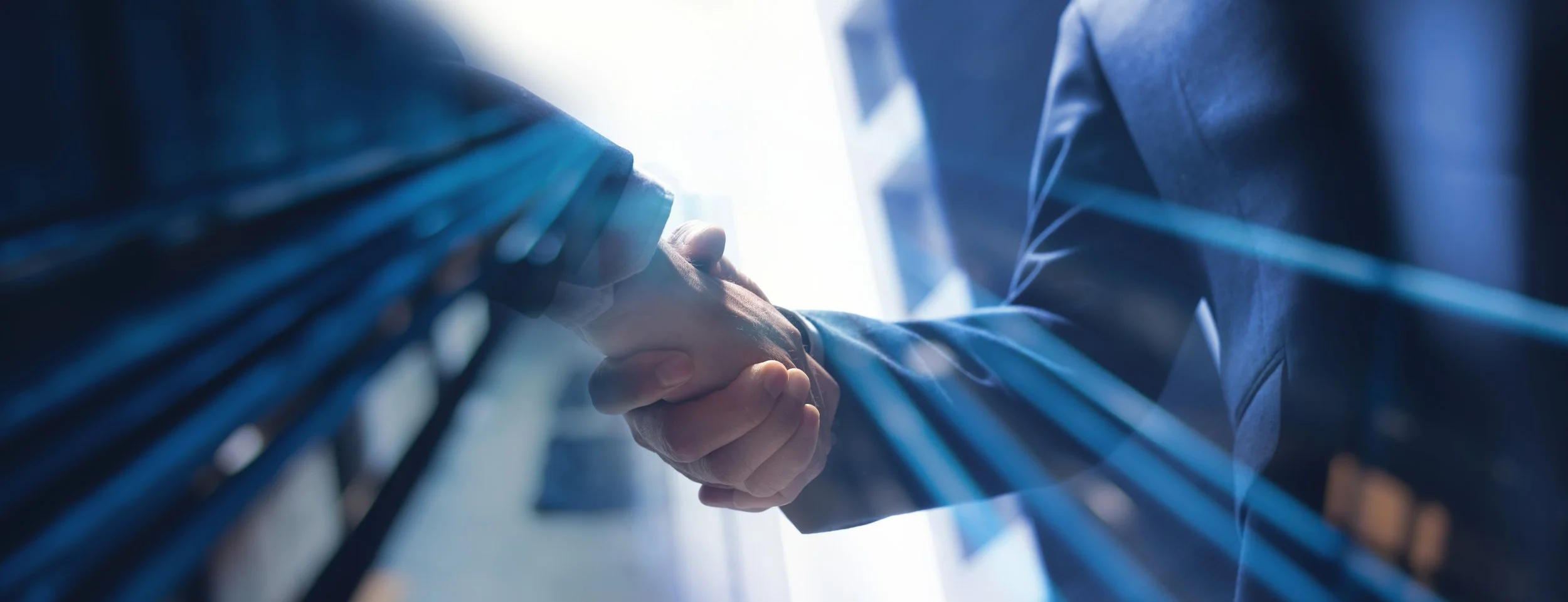 Two people shaking hands, seen through a glass wall with reflections, in a professional setting.