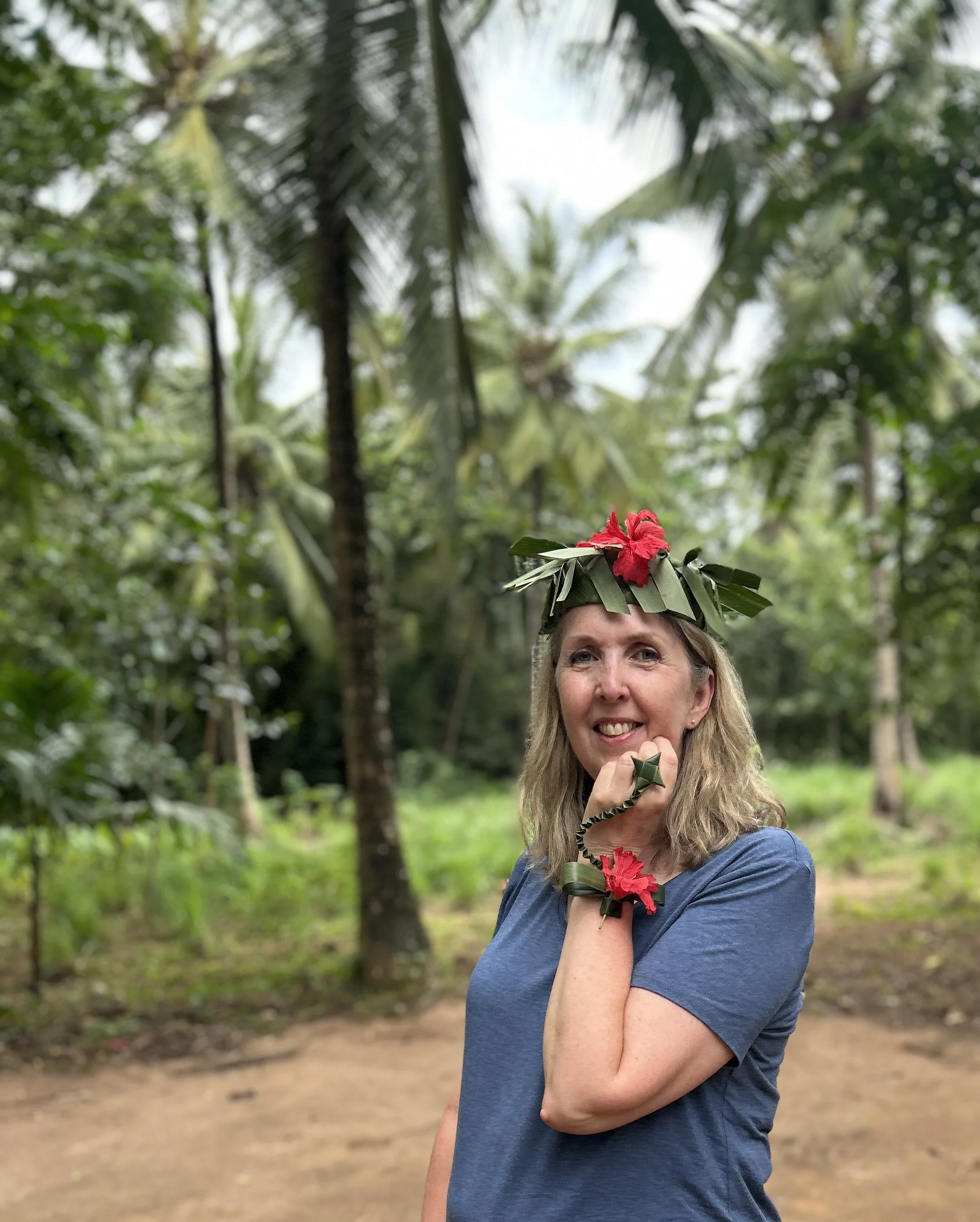 A woman wearing a crown made of leaves and flowers, with a matching bracelet and ring, standing outdoors in a lush, tropical forest in Zanzibar, Tanzania.