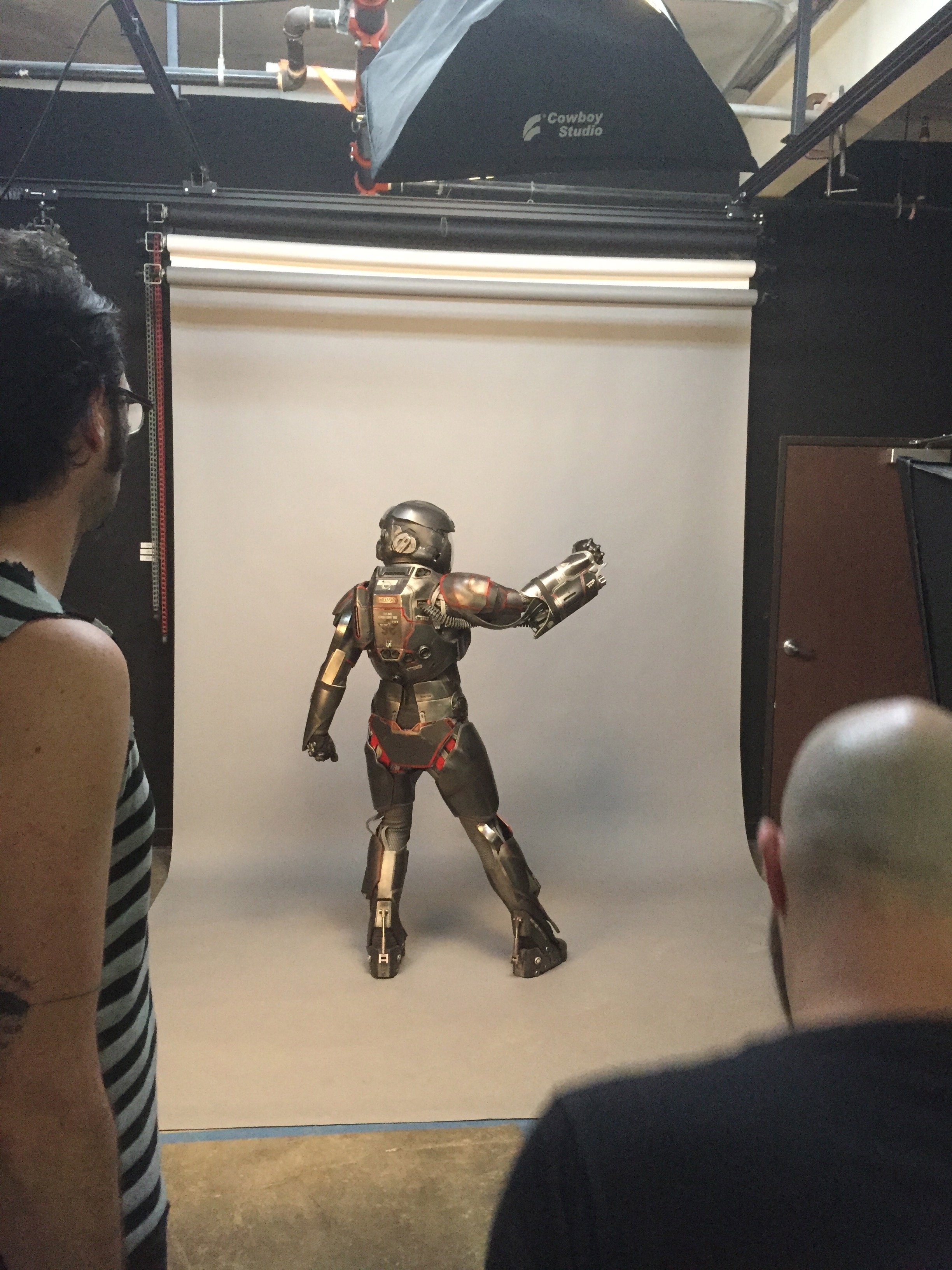 People observing a tam robot suit on a gray background with photography equipment overhead.