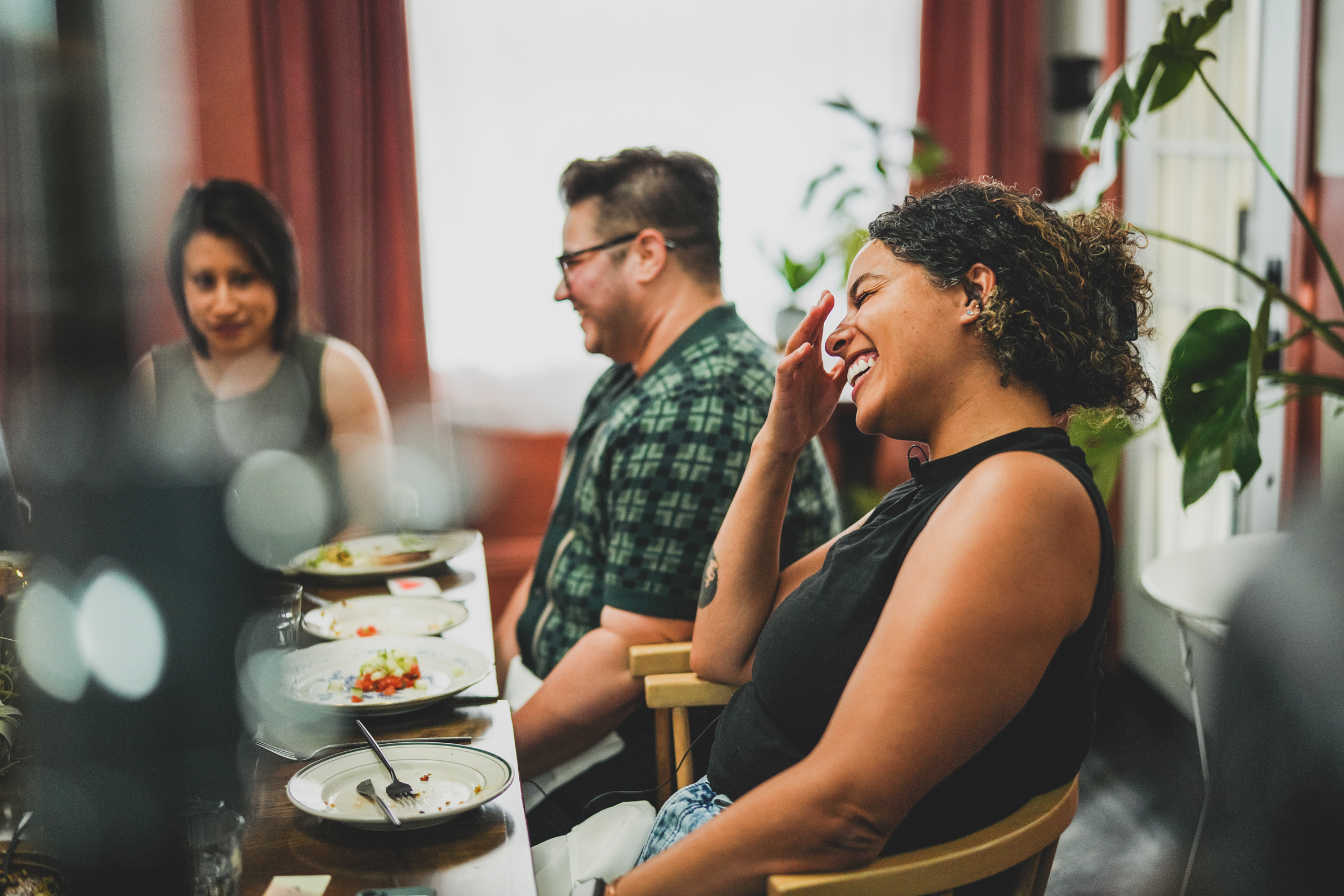 Three people sitting at a dining table, smiling and laughing, with empty plates and partially eaten food.