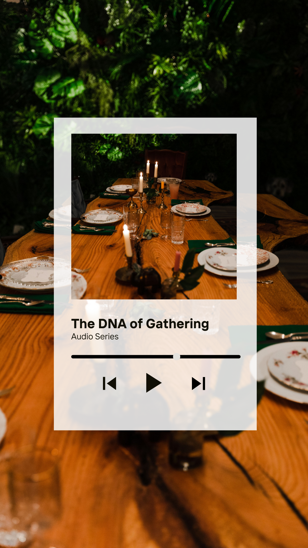 A wooden dining table decorated with lit candles, set with plates and glasses, surrounded by dark green foliage.