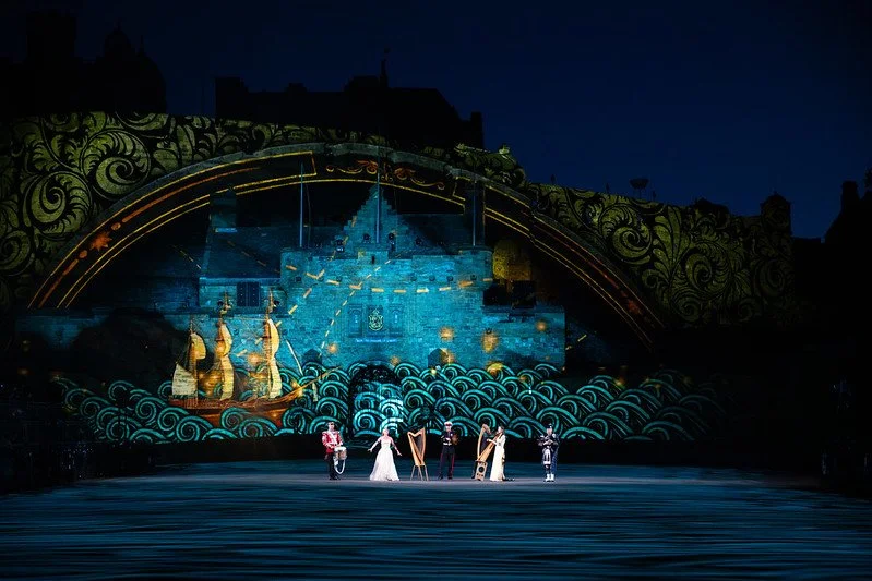 A stage with a projection of a castle and ships, featuring seven performers in costumes in front.