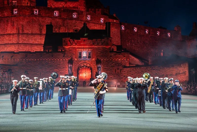 Military band performing in front of Edinburgh Castle at night, illuminated in red.