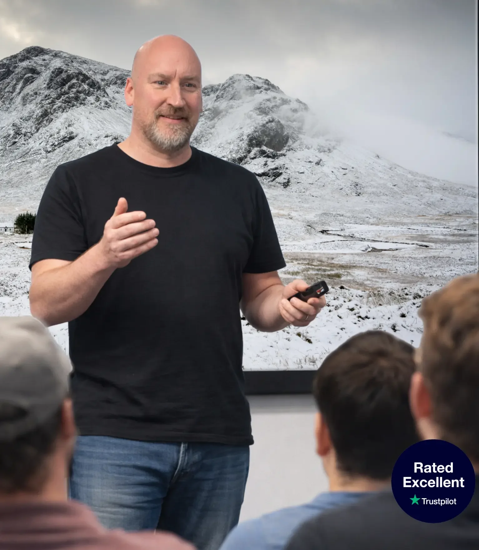 Man giving a presentation to a group with a snowy mountain backdrop in a room.