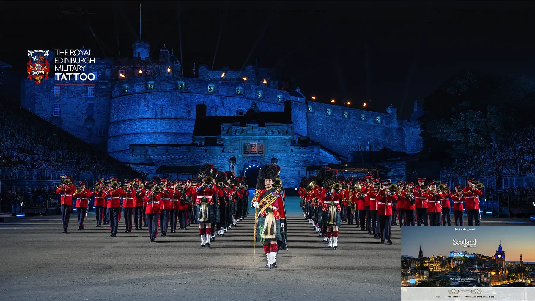 A nighttime military parade with soldiers in traditional Scottish dress and red jackets performing in front of Edinburgh Castle illuminated at night.