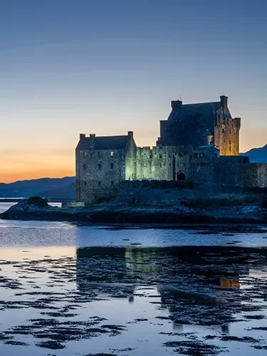 A historic castle on the coast during sunset with reflections in the water.