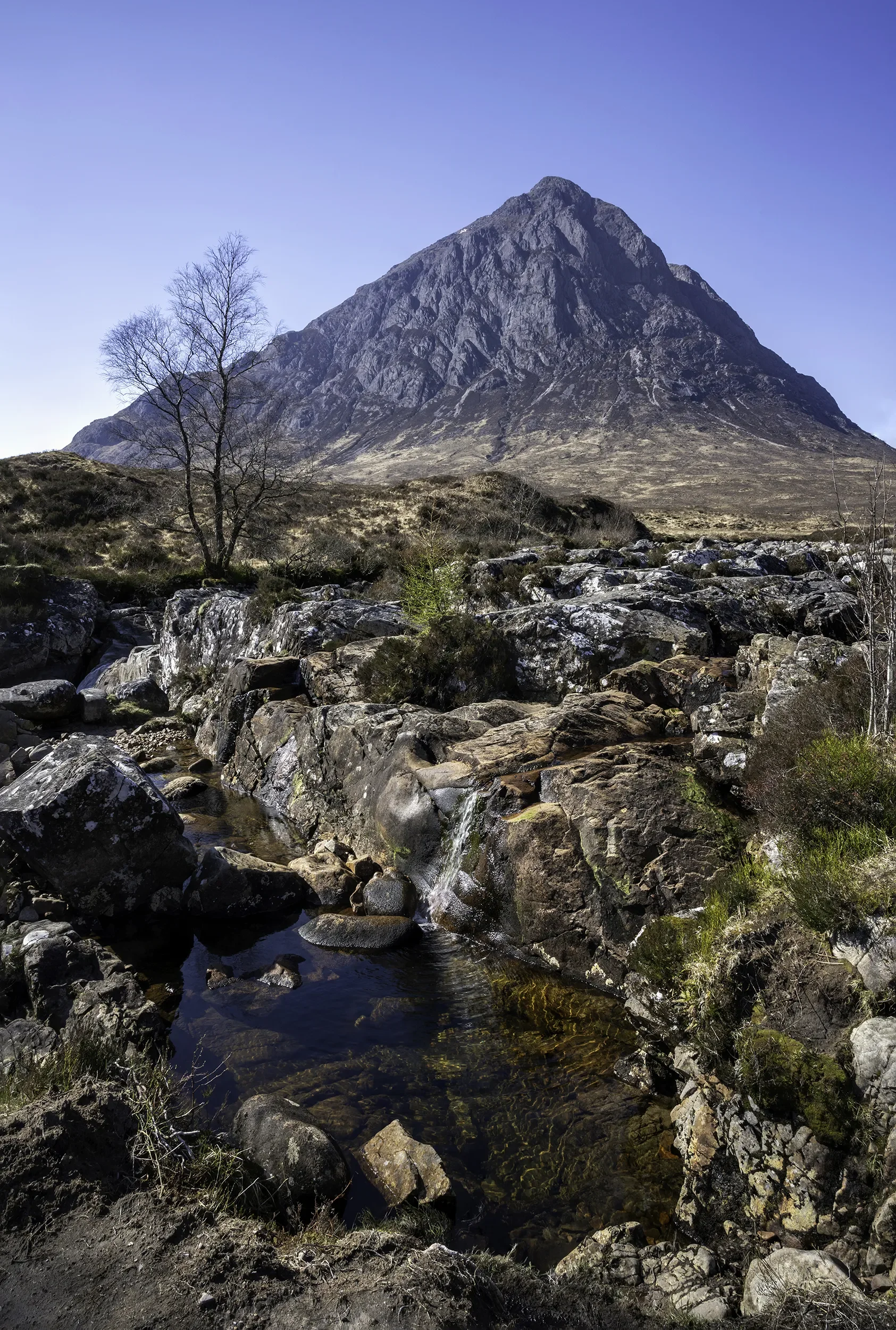 A historic street leading up to Edinburgh Castle on a hill, with stone buildings, stairs, and modern street lamps.