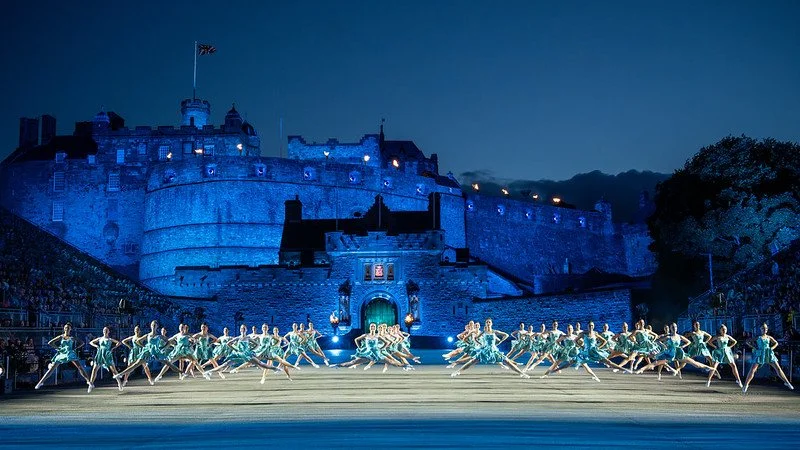 Nighttime outdoor ballet performance with dancers in teal costumes in front of a lit castle.