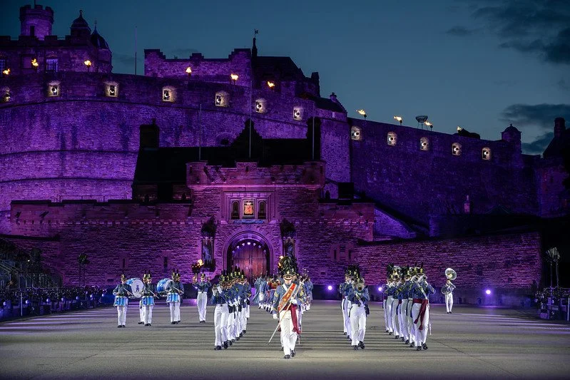 A military parade taking place at night in front of a large, illuminated castle.