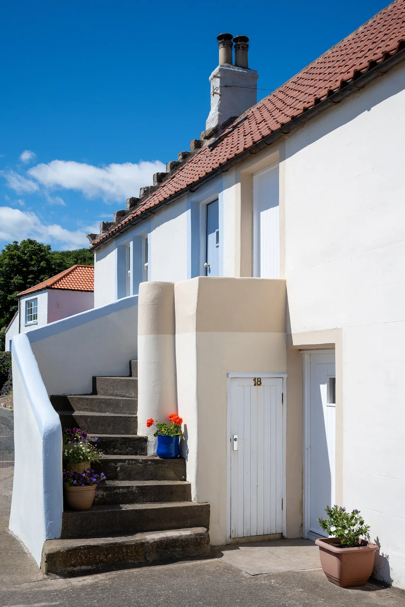 White house with red tile roof, blue sky, and potted flowers on stone stairs leading to the entrance.