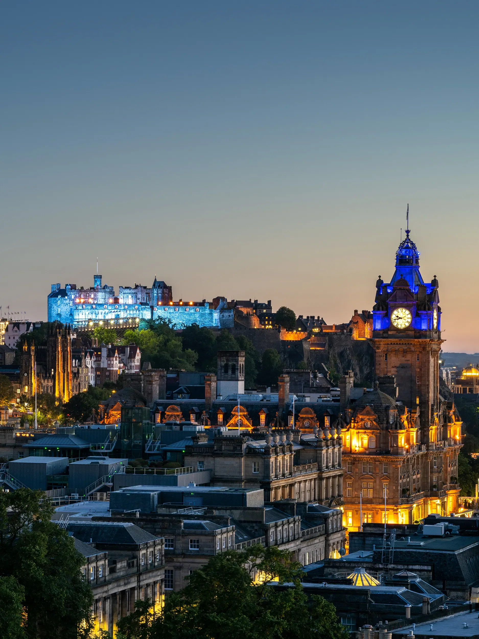 A large stone monument resembling two upright stones leaning towards each other, situated in a grassy, mountainous landscape with cloudy skies overhead.