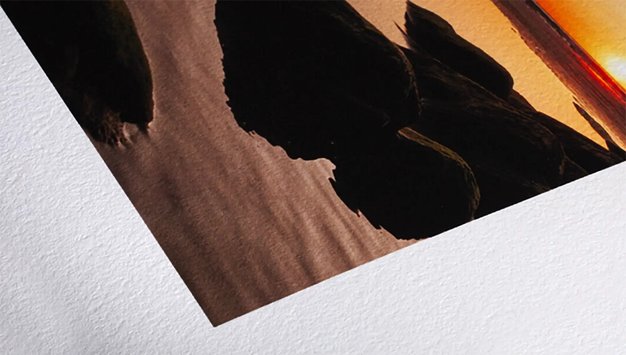 A printed poster or photograph of a desert landscape during sunset with silhouetted rocks or dunes.