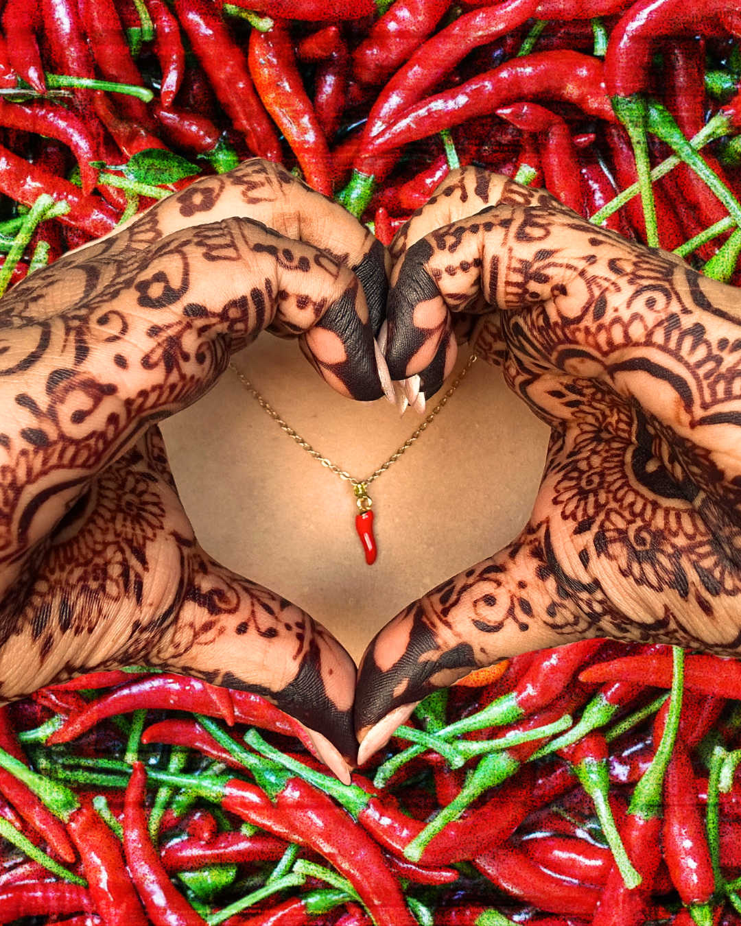 Red chilli pepper pendant necklace framed by mehndi-decorated hands forming a heart shape.