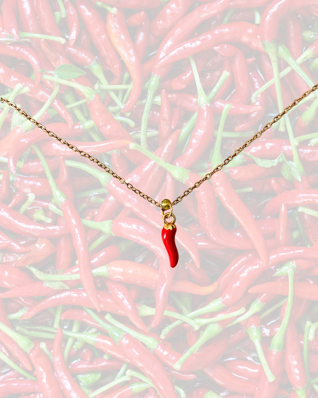 Gold-tone chilli pepper necklace with a miniature red chilli charm displayed against a background of red peppers.