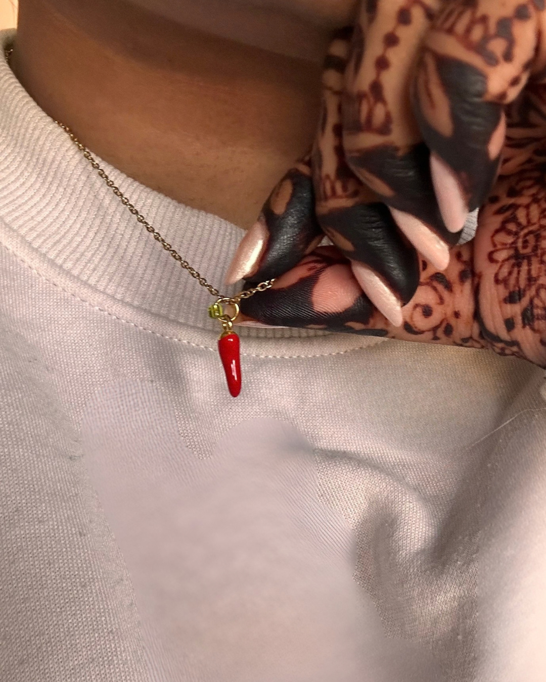 Close-up of a red chilli pepper charm necklace worn with a white top and traditional mehndi designs.