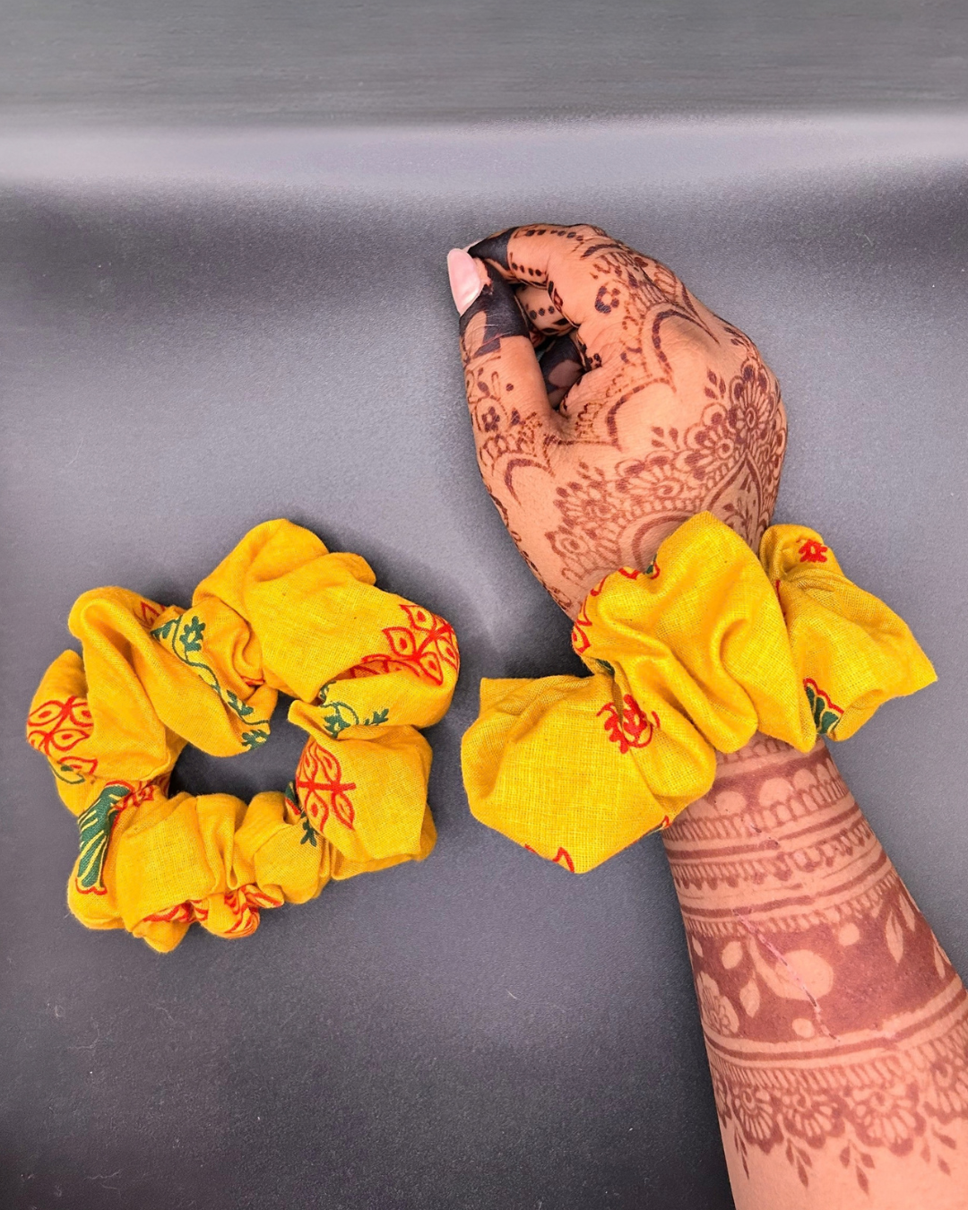 Bright yellow printed fabric scrunchie with red and green motifs, shown on wrist