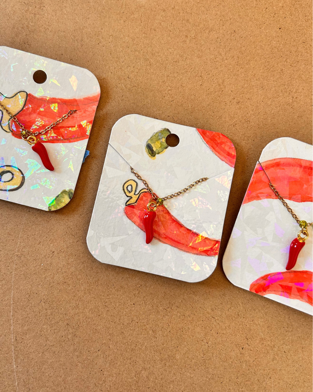 Three red chilli pepper necklaces displayed on illustrated jewellery backing cards.