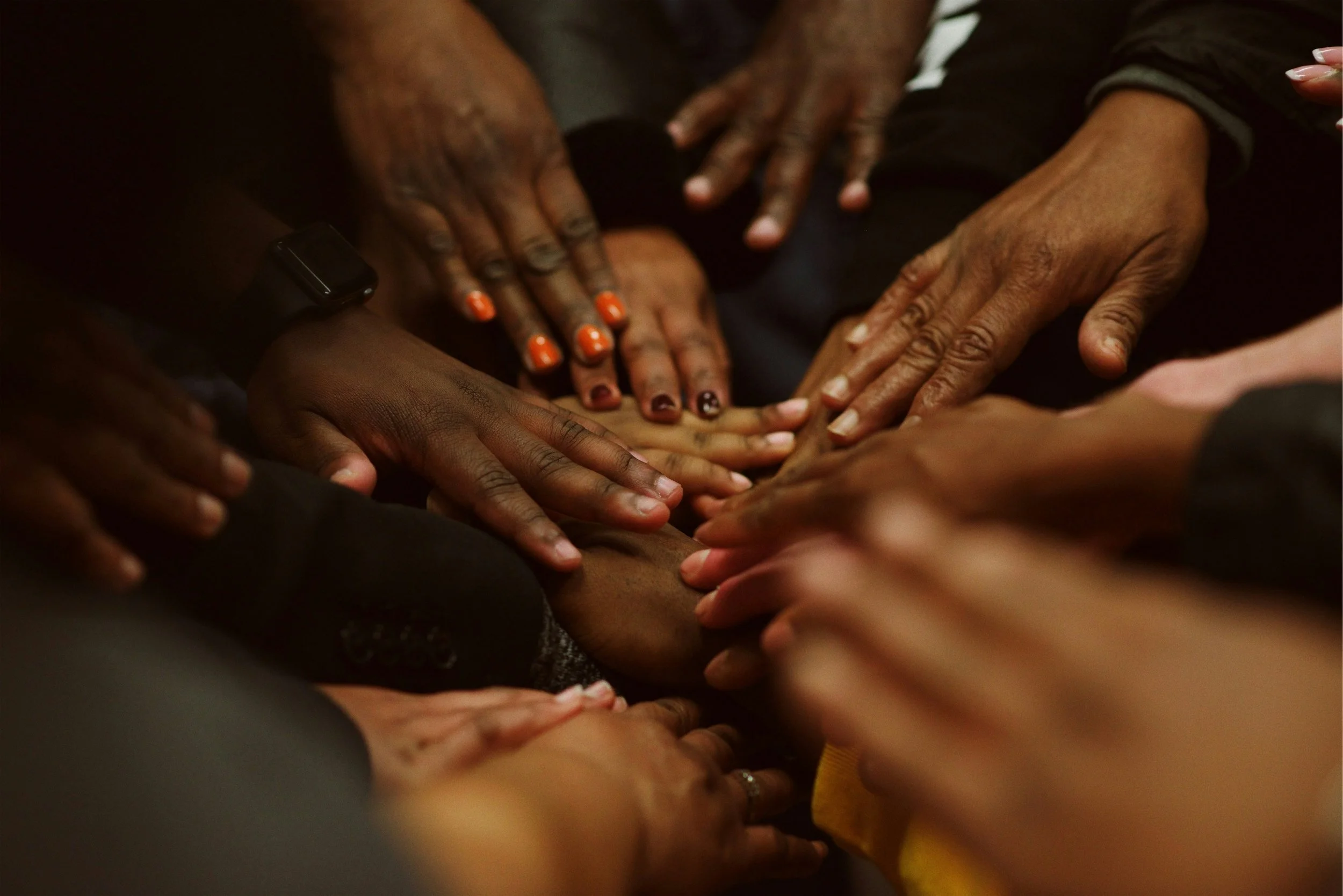 Multiple hands of different skin tones reaching towards the center, creating a unified gesture of connection and solidarity.