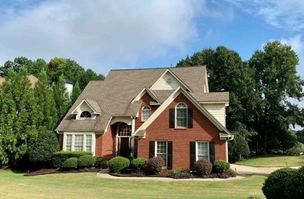 A large, two-story house with a brick and siding exterior, multiple gable roofs, and black shutters, surrounded by a well-maintained lawn and bushes.