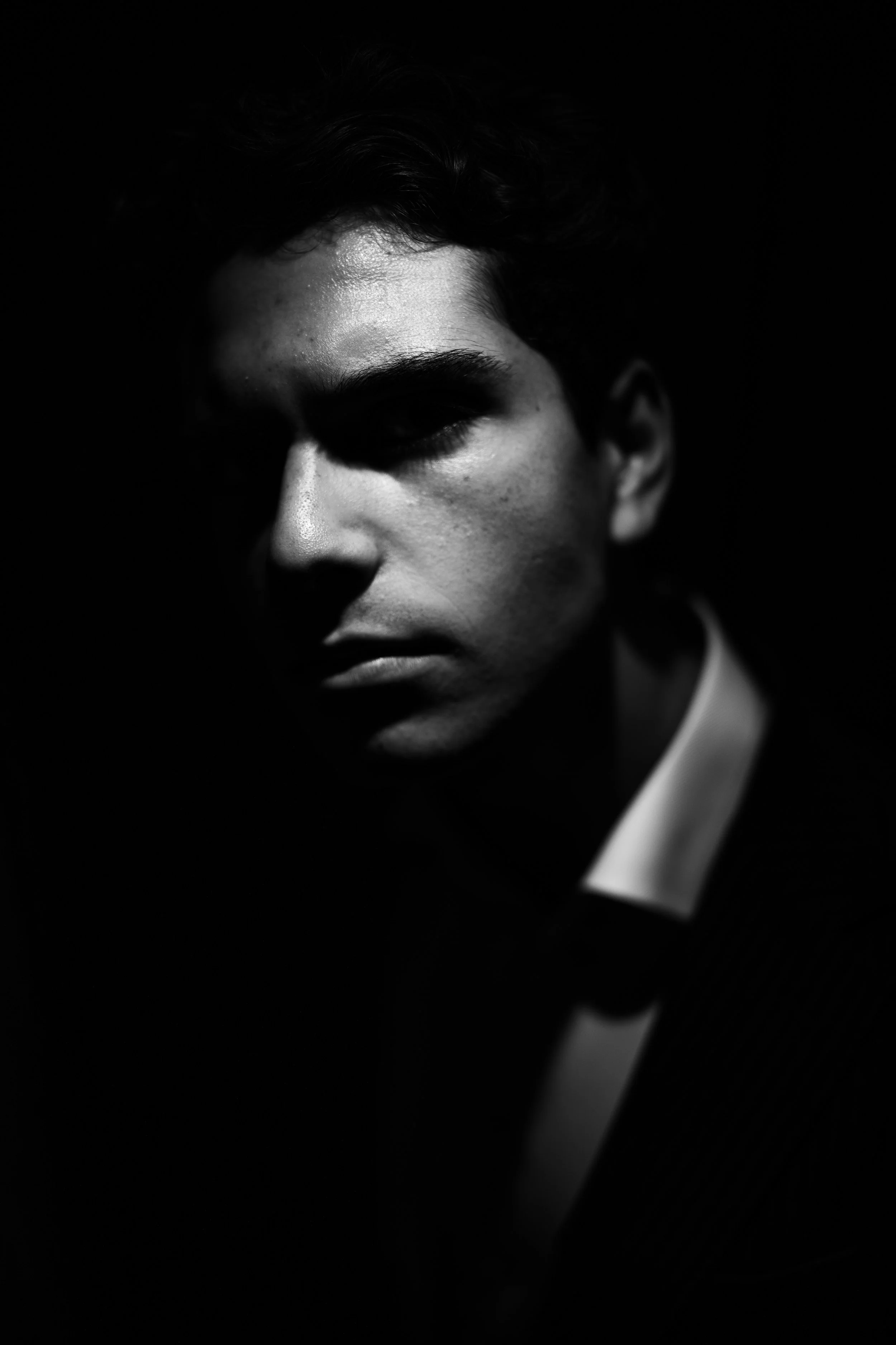 Black and white portrait of a young man with short dark hair, wearing a tuxedo and bow tie, with dramatic lighting highlighting his facial features.