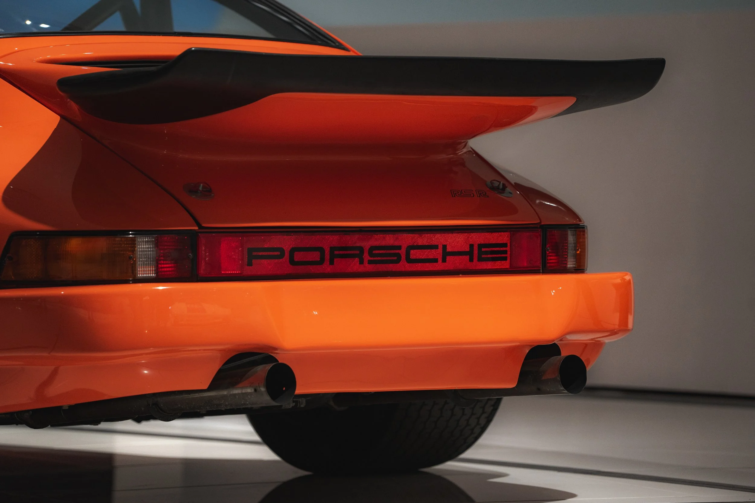 Rear view of an orange Porsche 911 Carrera with a prominent rear wing and dual exhaust pipes.