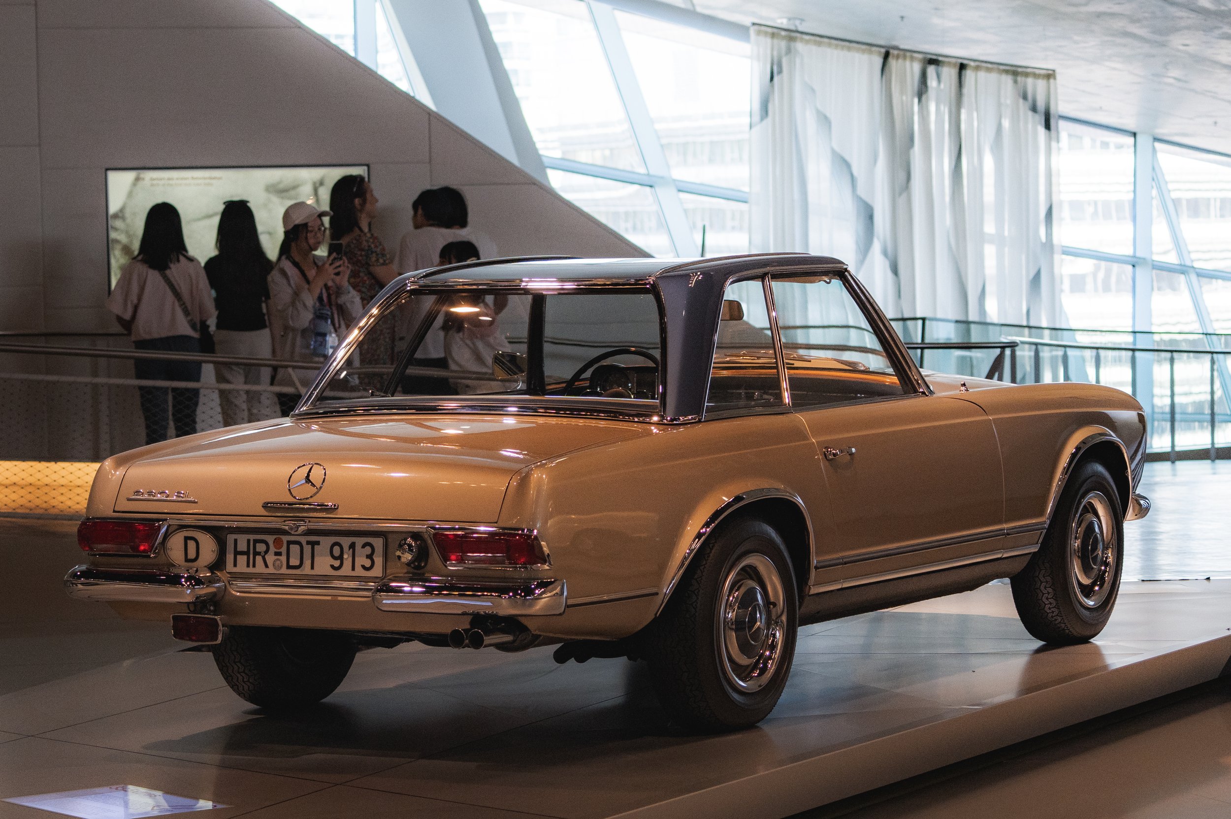 Vintage Mercedes-Benz car displayed in a modern museum with visitors in the background.