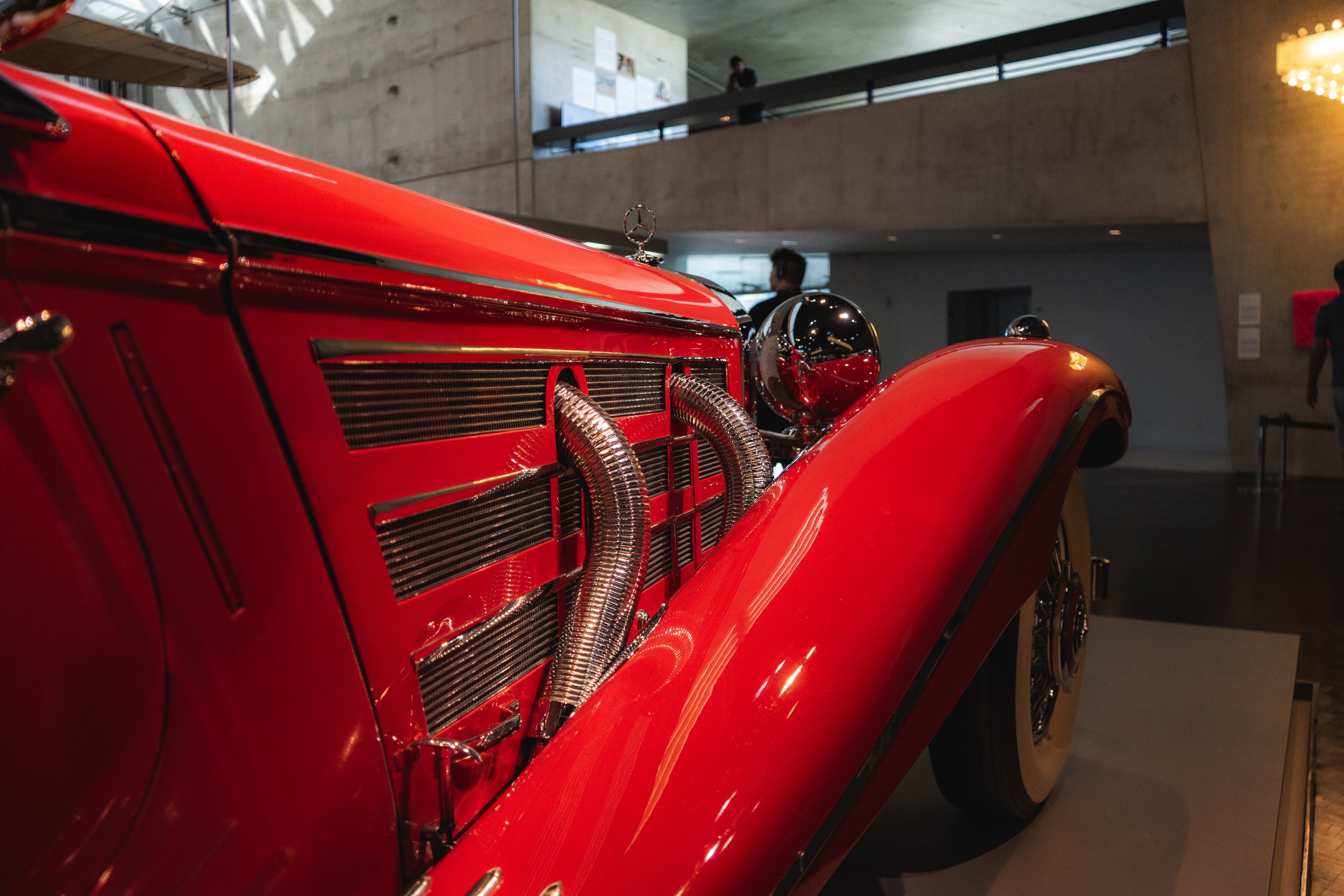 Close-up of a vintage red race car on display in a museum, with a focus on the front bodywork, chrome details, and passenger side fender.