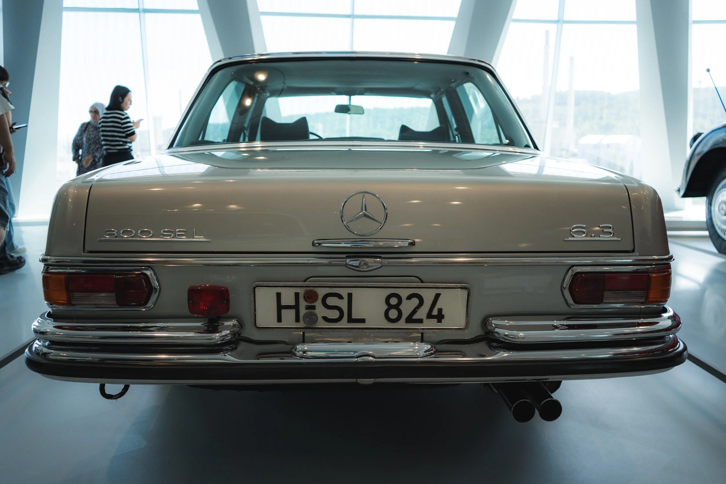 Rear view of a vintage Mercedes-Benz 300 SEL 6.3 car in a museum, with license plate 'H SL 824' and visible Mercedes logo.