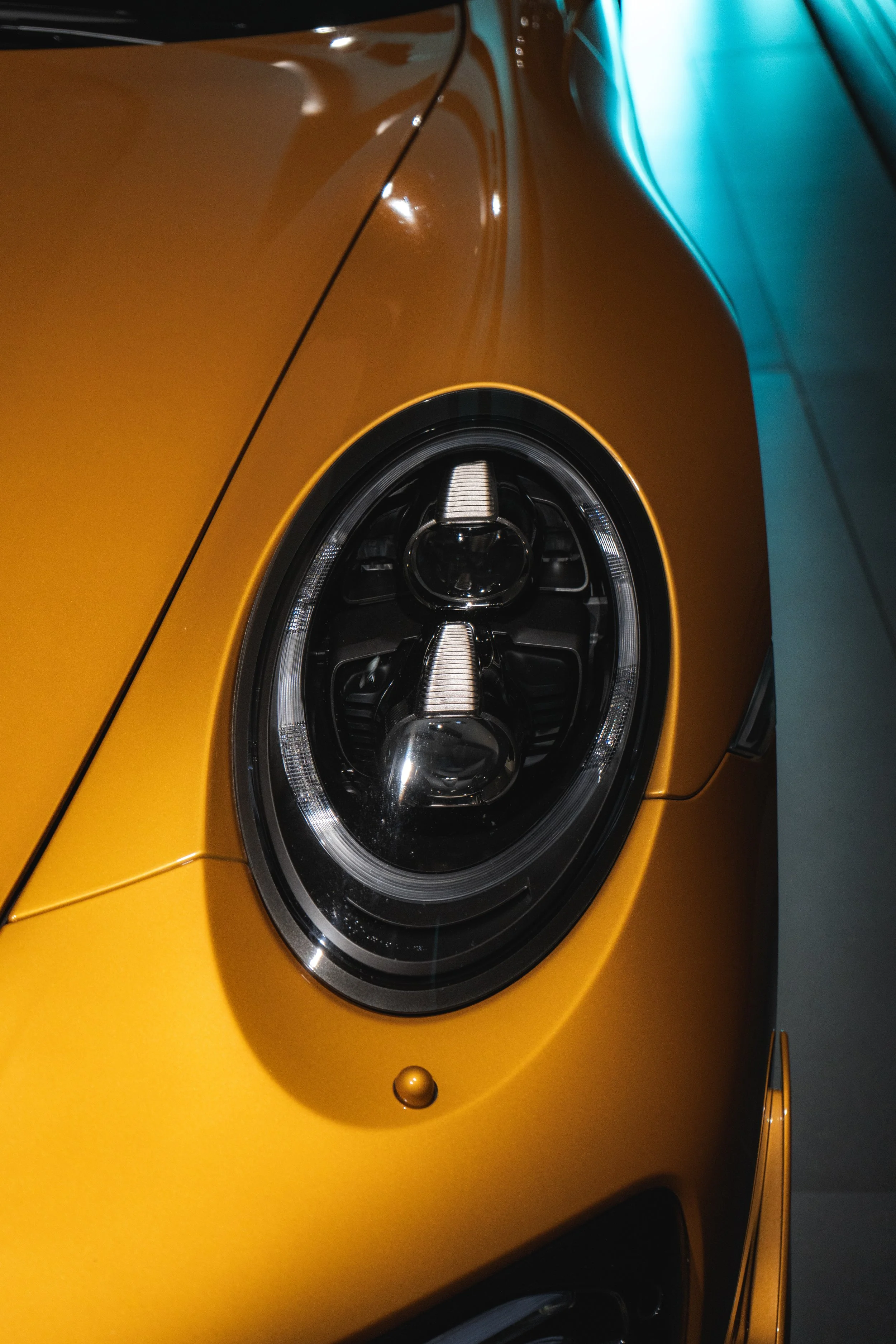 Close-up of the front left side of a yellow sports car, showing the headlight and part of the hood and fender.