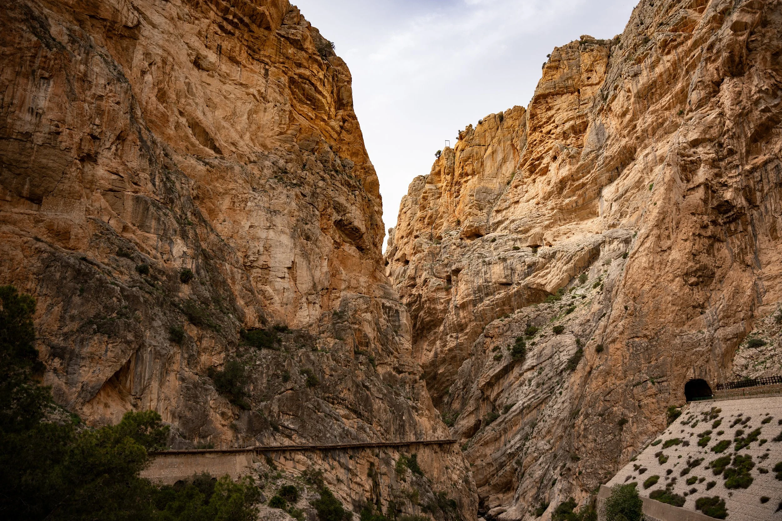 A narrow canyon with steep rocky walls and a concrete road or path along the side.