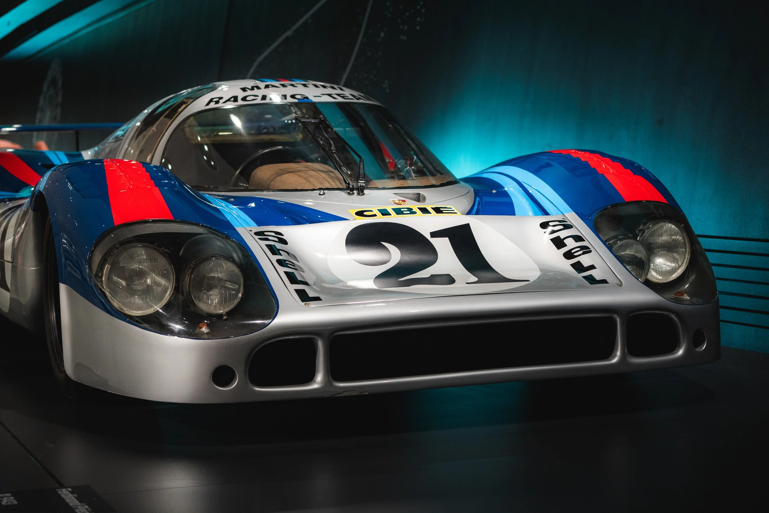 A classic race car with the number 21, primarily silver with blue and red accents, displayed in a museum setting.
