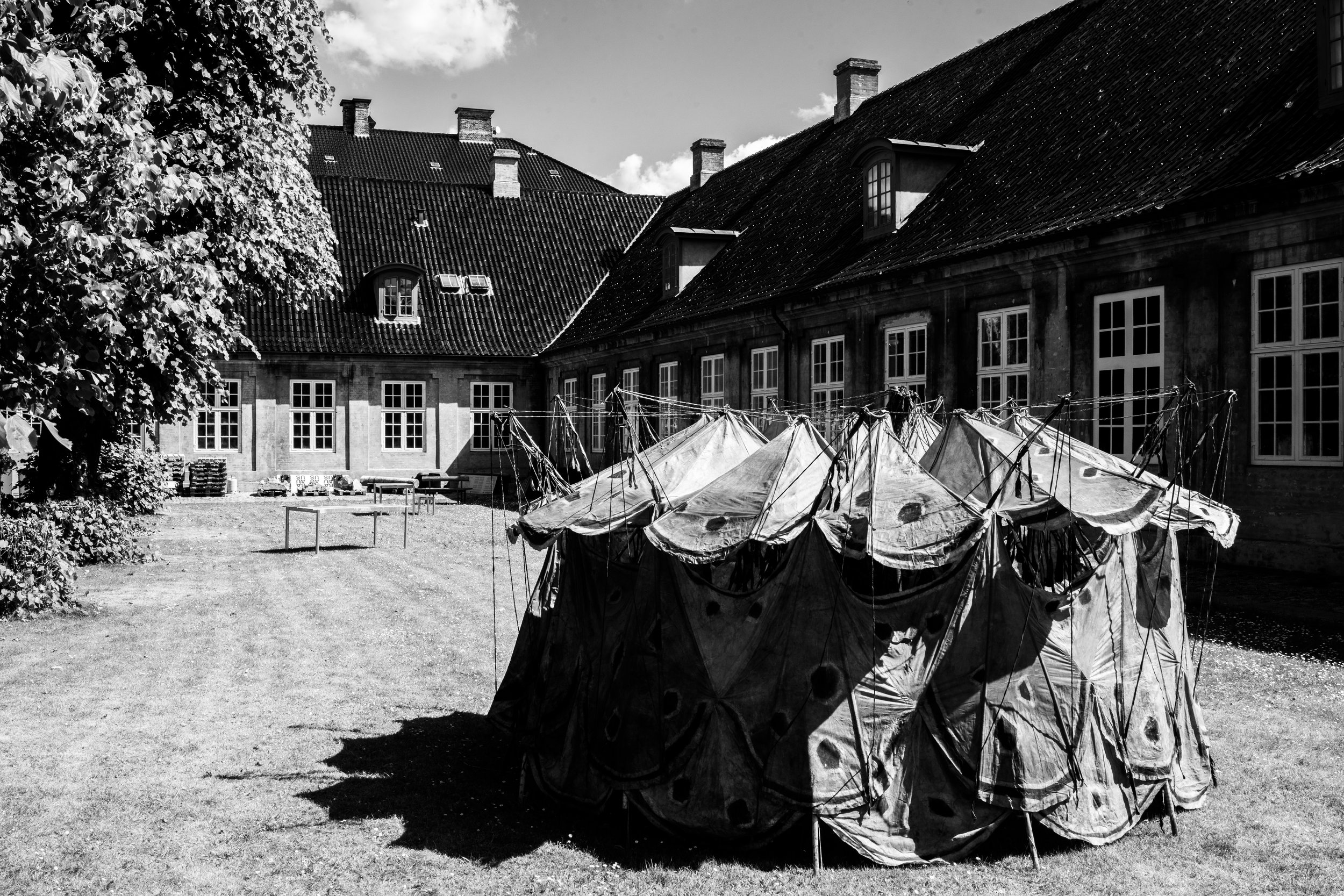 Black and white photo of a large outdoor tent in a courtyard with old building in the background.