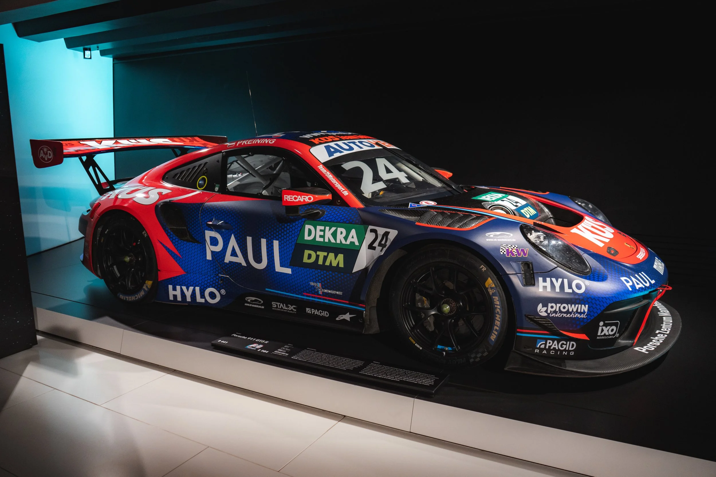 A race car on display in a gallery with sponsorship logos and racing decals