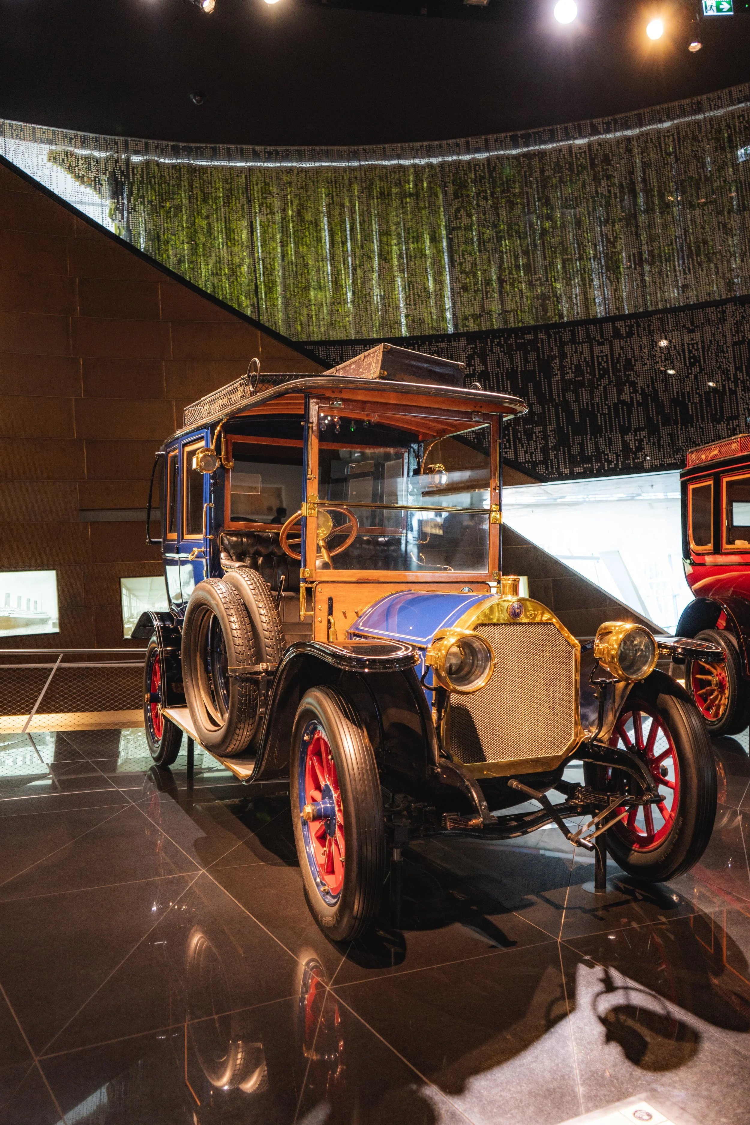 Vintage automobile displayed indoors with reflective black tiled floor and modern ceiling lights.