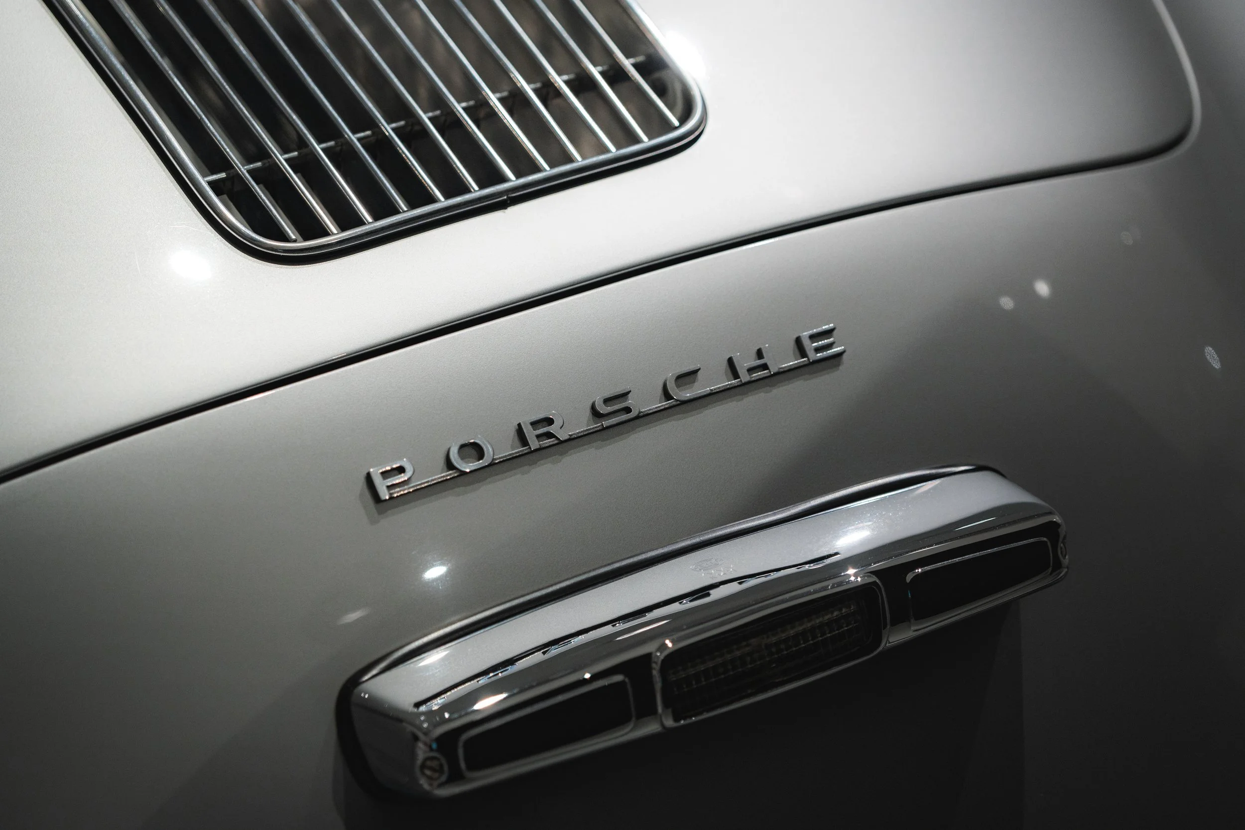 Close-up of the front of a vintage silver Porsche sports car, showing the Porsche emblem and part of the grille.