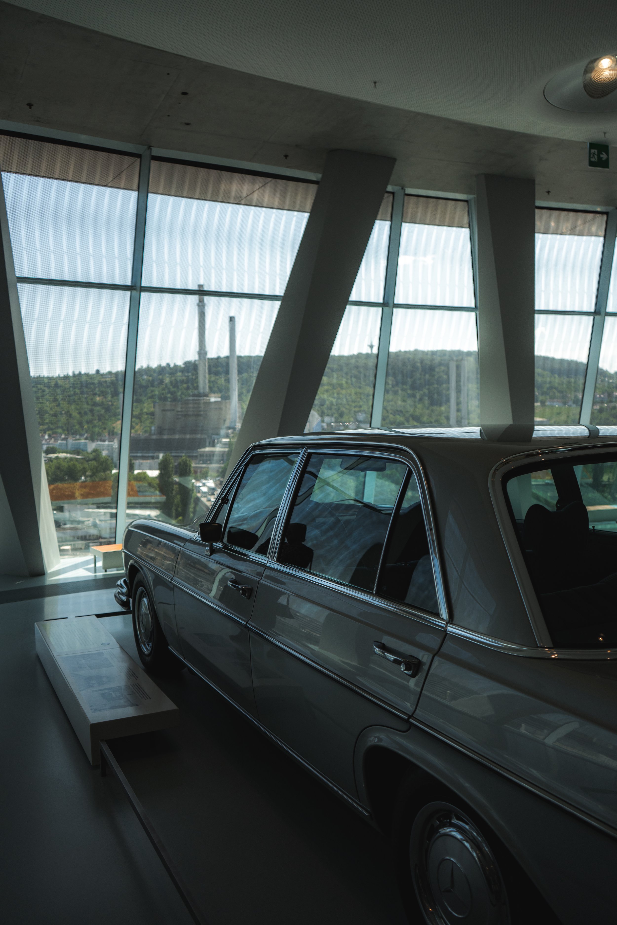 A vintage Mercedes-Benz car displayed inside a modern building with large glass windows showing an outdoor view of hills and industrial chimneys.