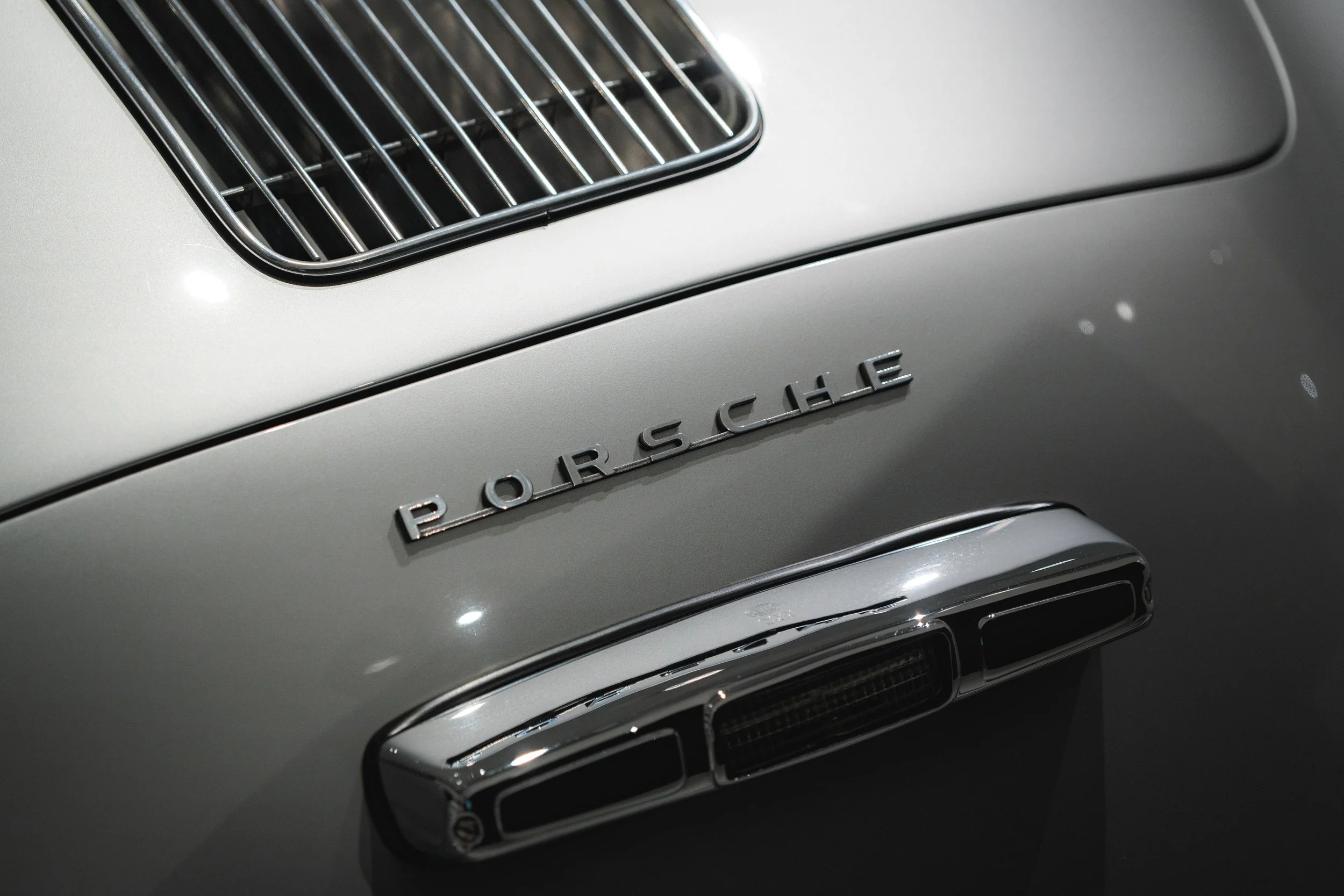 Close-up of a vintage Porsche car with silver paint, showing the Porsche emblem and part of the front grille.