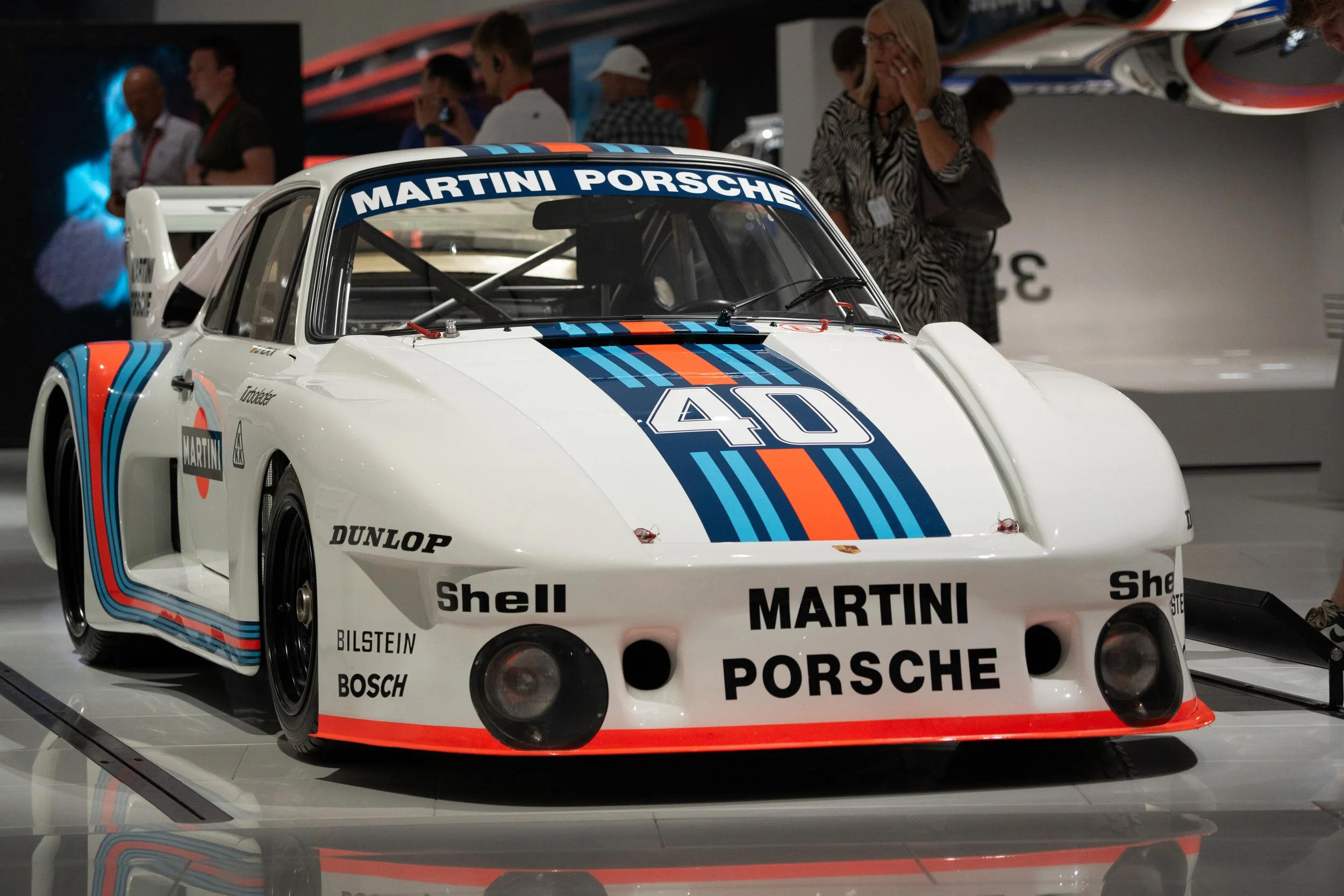 A vintage Martini Porsche race car on display at a car show, white with Martini racing stripes and sponsor logos.